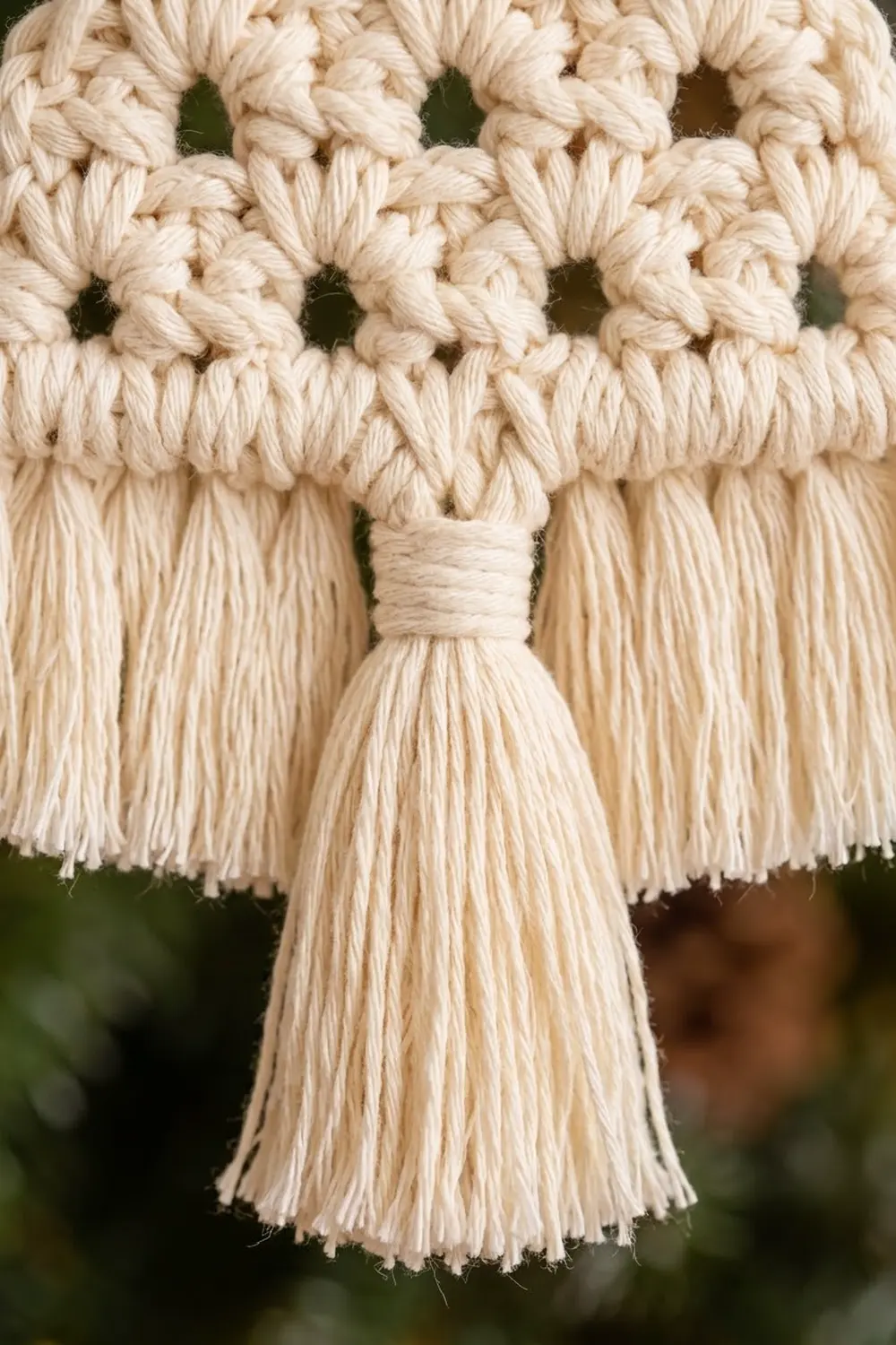 Close-up of cream-colored macramé wall hanging with knotted pattern and tassel fringe detail.