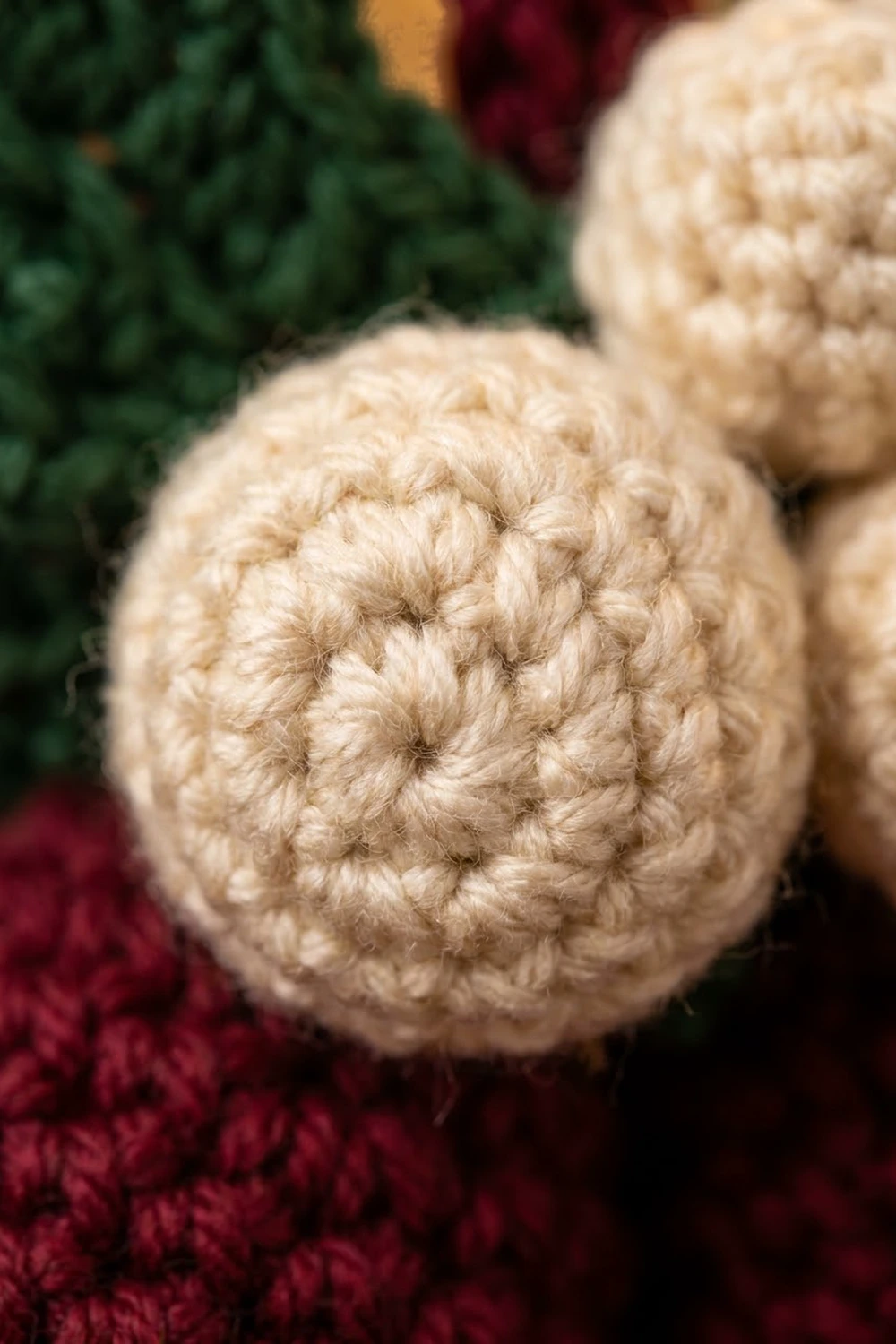 Close-up of cream-colored crocheted ornaments with detailed stitching displayed on burgundy and green holiday decor.