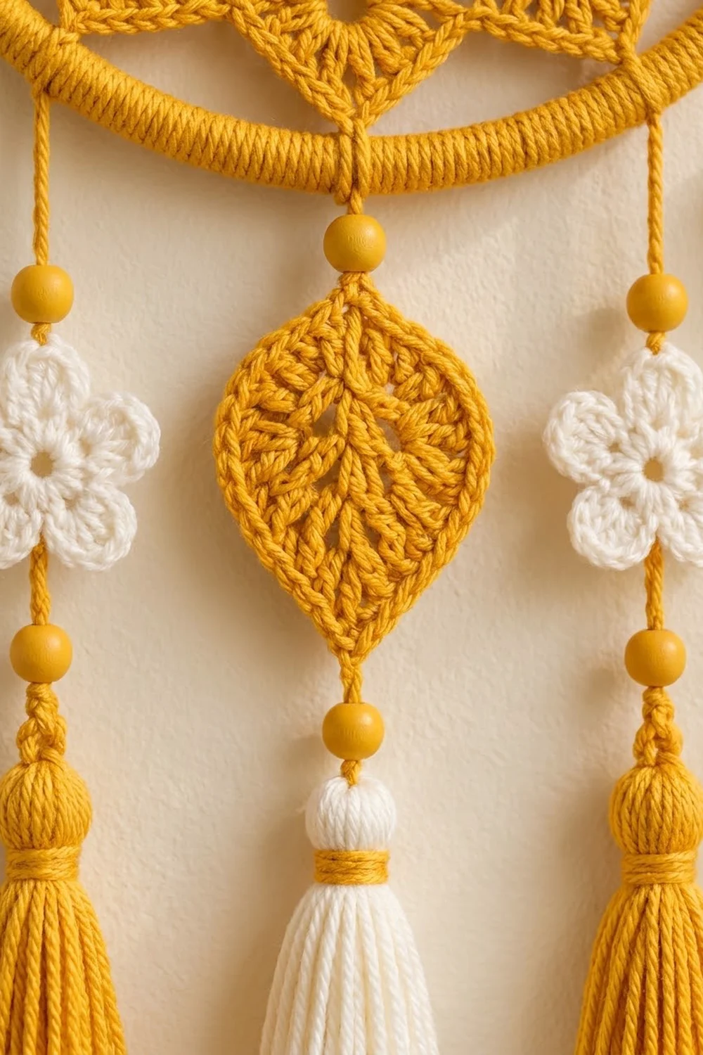 A handmade macramé wall hanging with golden yarn, white crocheted flowers, wooden beads, and tassels.