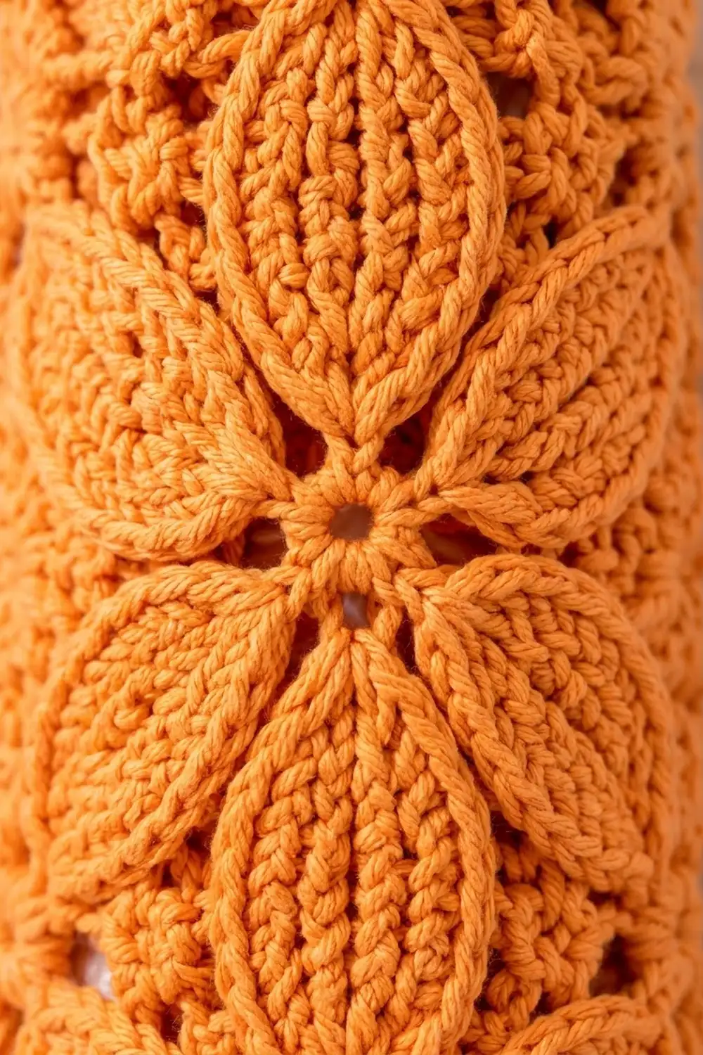 Close-up of orange crocheted fabric showing intricate cable knit texture with decorative openwork pattern details.