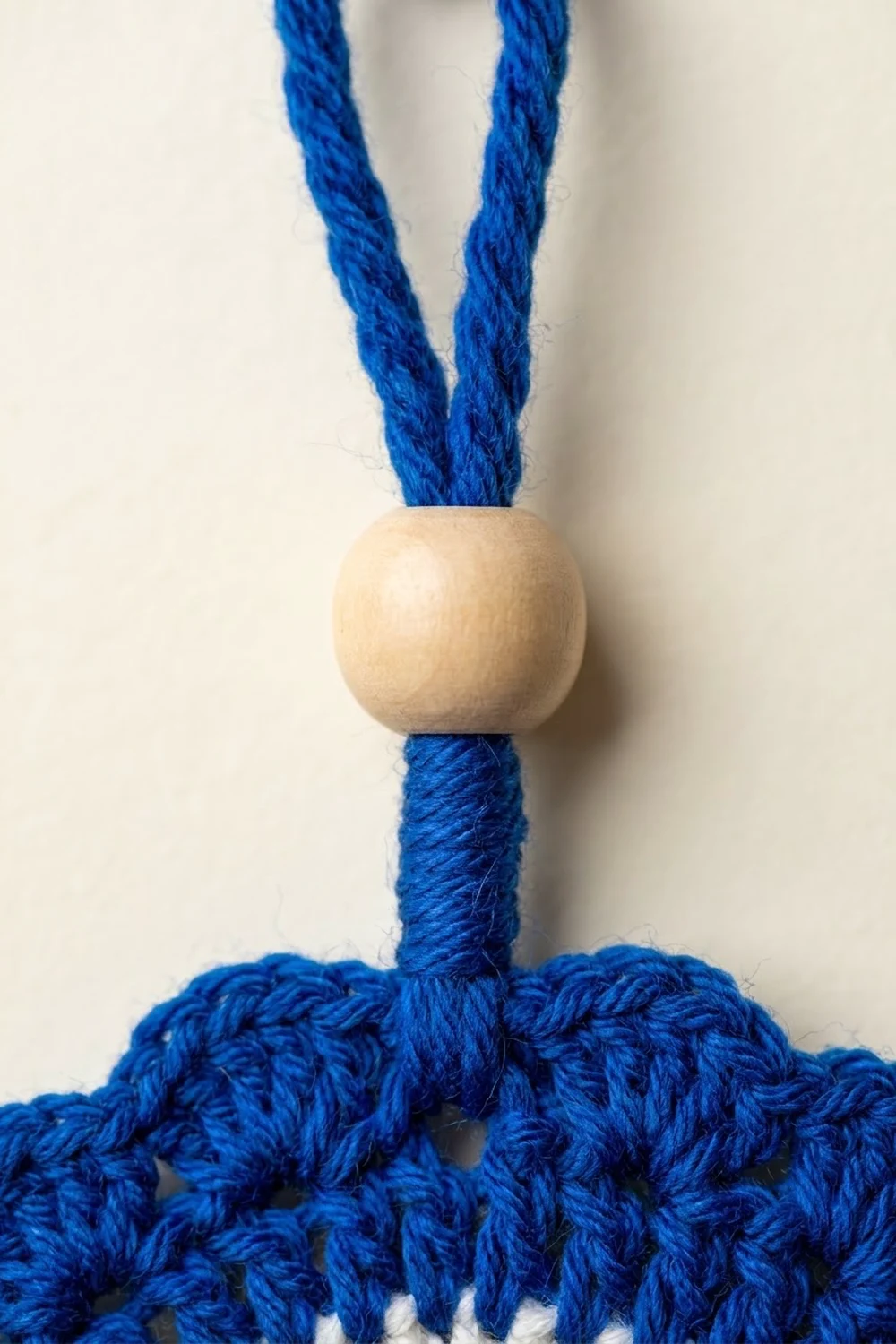 A wooden bead threaded onto blue twisted rope with frayed ends against a white background.