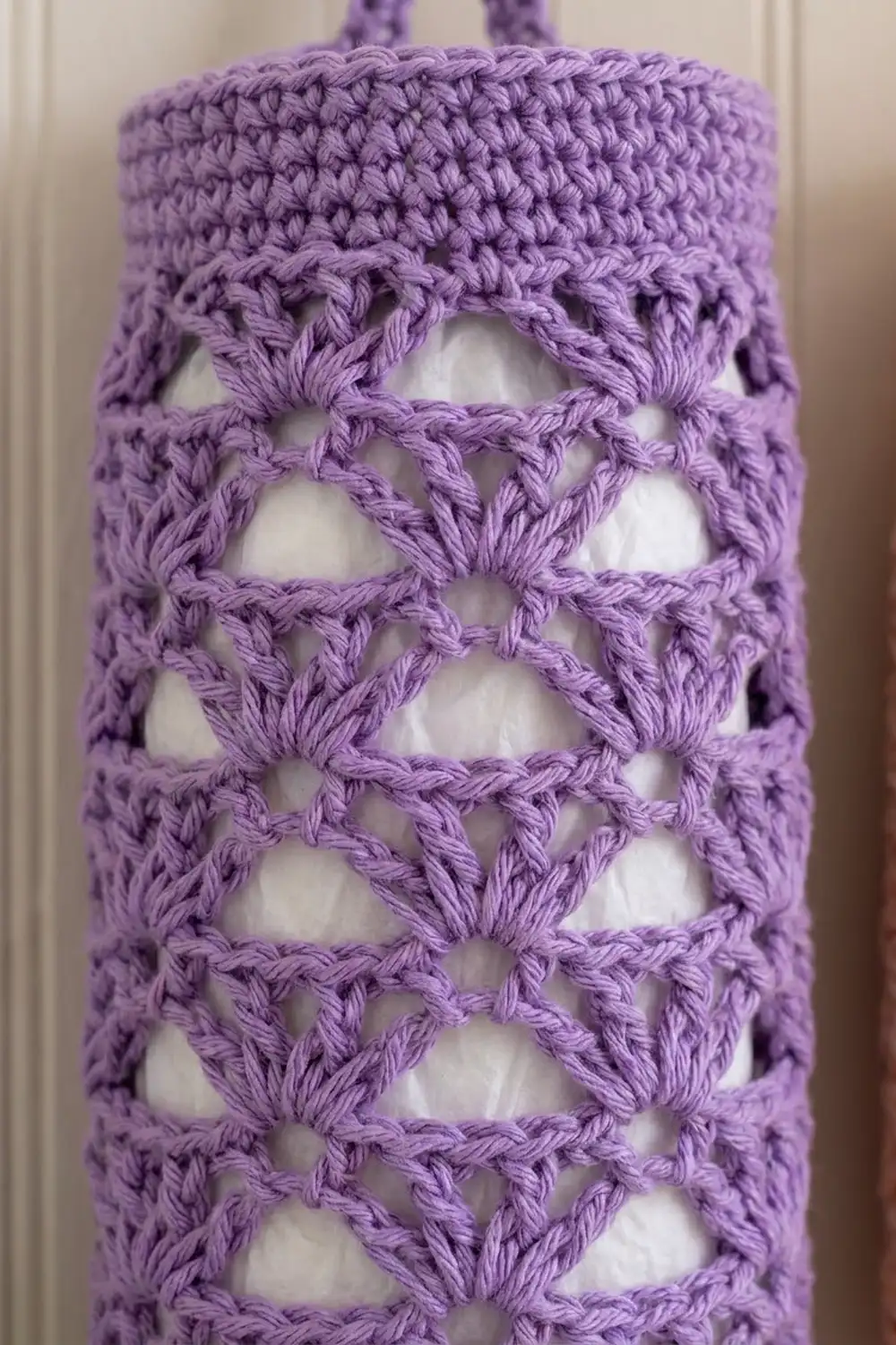 Close-up of a purple crocheted bag with an open lattice pattern and handles visible at the top.