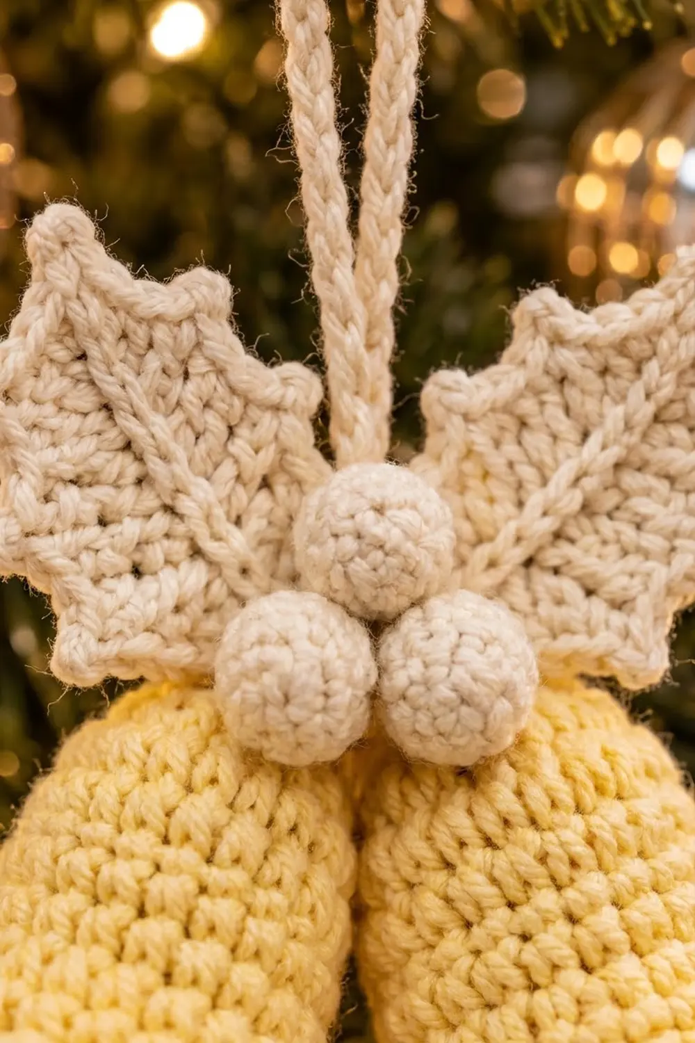 A crocheted ornament featuring a cream star with white rope accents and pale yellow pom-poms against golden lights.