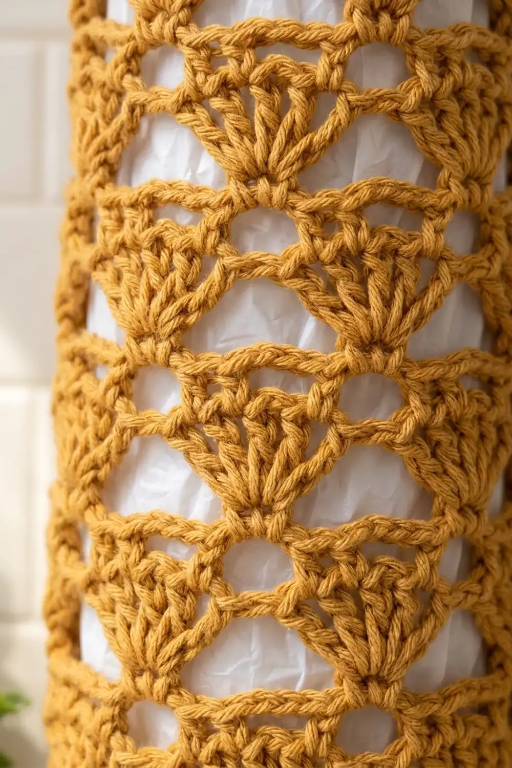 Close-up of golden yellow crocheted fabric with openwork diamond pattern and visible twisted stitches against a blurred white background.