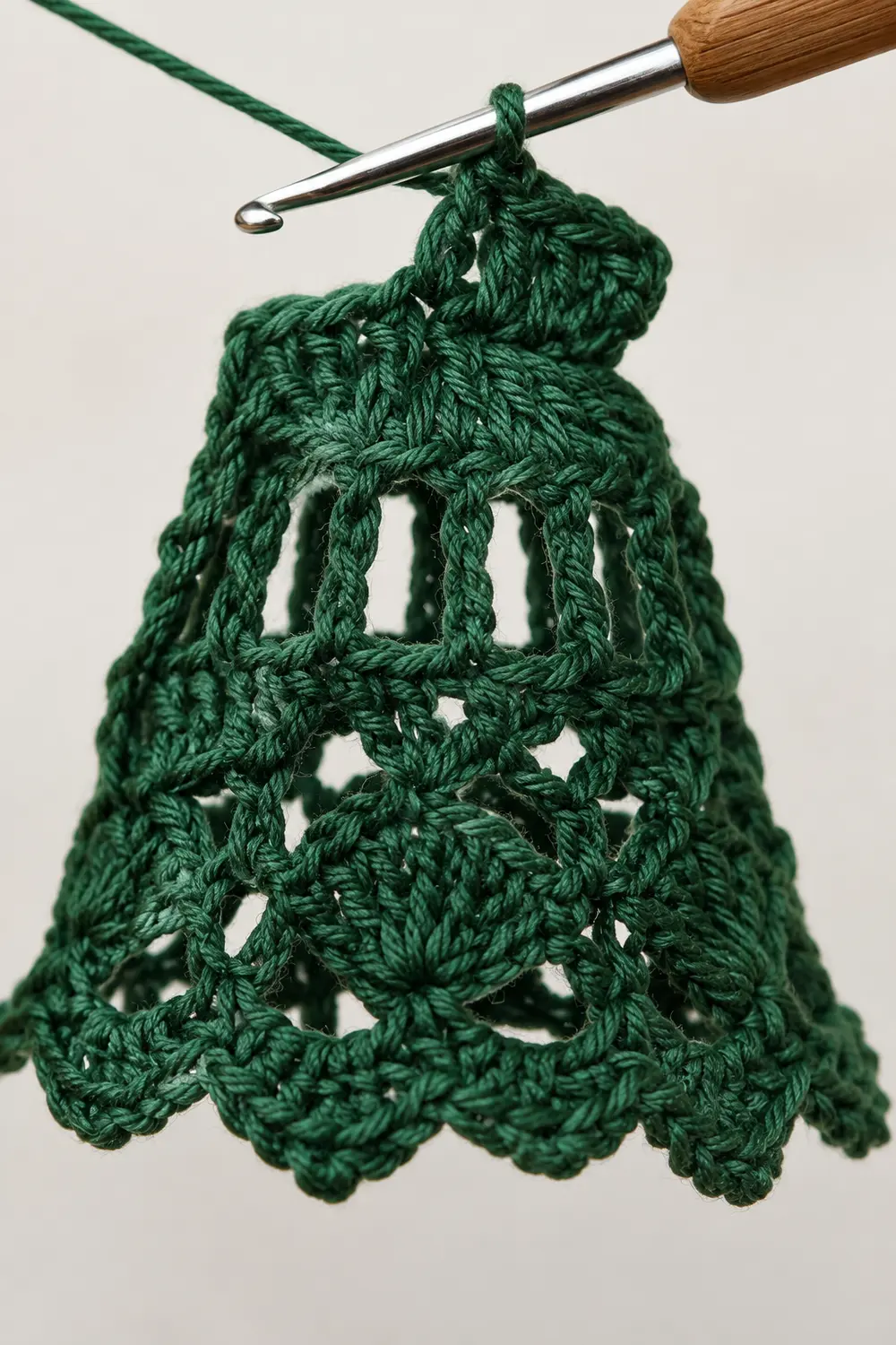 A green crocheted lace doily hangs from a wooden crochet hook against a white background.