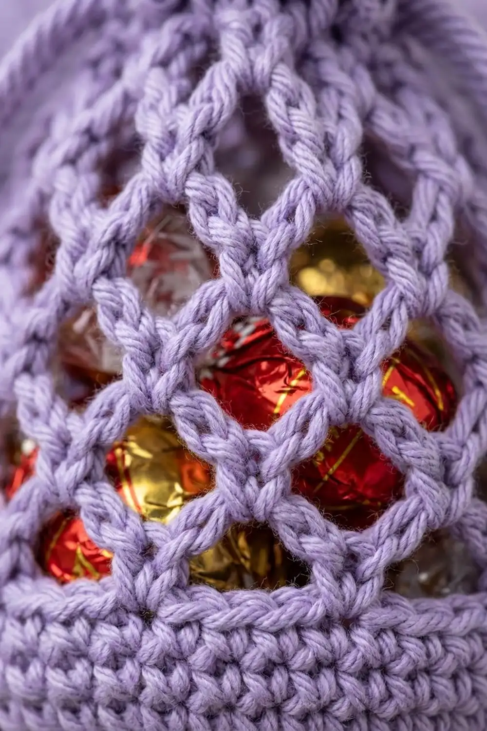 Close-up of lavender crocheted mesh with red and gold beads woven through the lattice pattern.