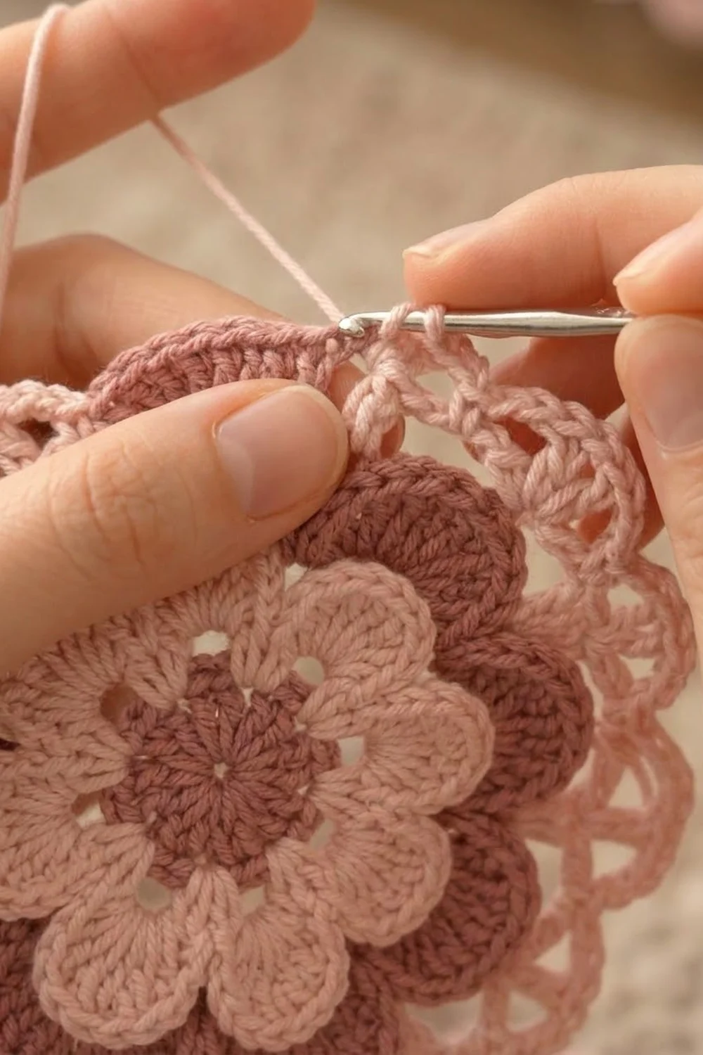Close-up of hands crocheting a dusty rose-colored lacy motif with a silver crochet hook.