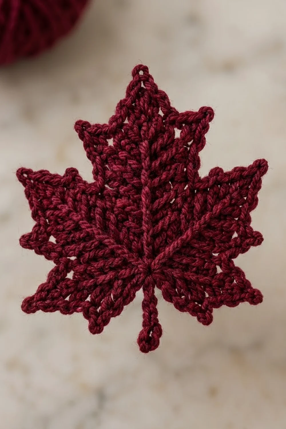 Burgundy crocheted snowflake with delicate openwork pattern against a soft, blurred beige background.