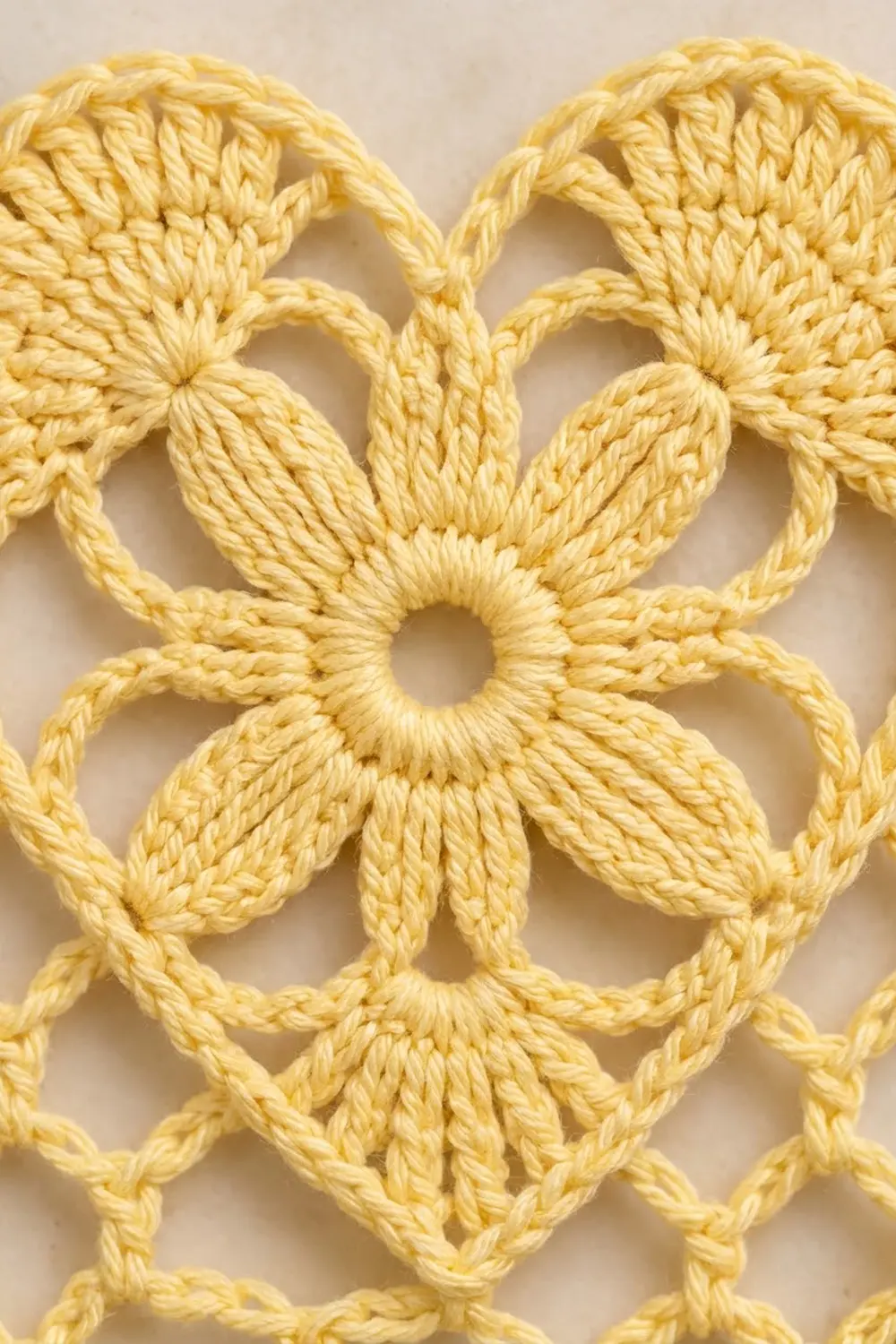 Pale yellow crochet fabric featuring dimensional flowers with textured petals and looped stitches on a white background.