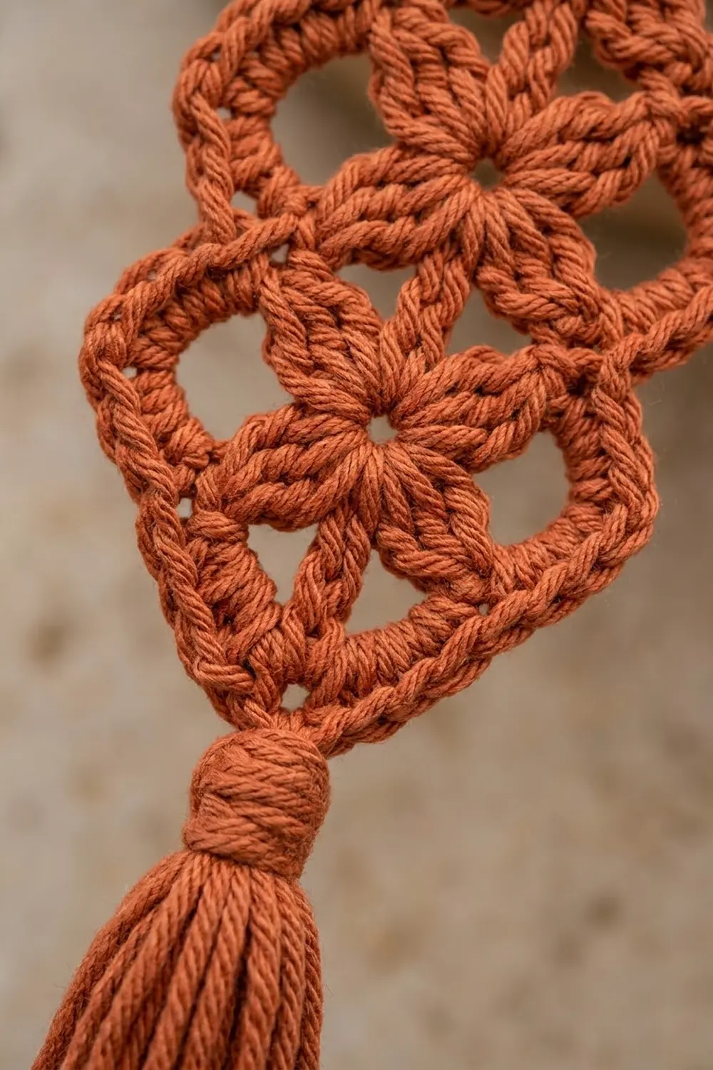 Close-up of rust-orange crocheted lace with interlocking loops forming a geometric lattice pattern.