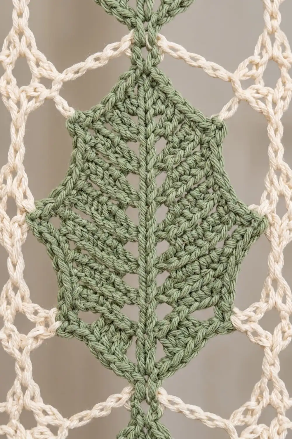 Close-up of sage green crocheted diamond motif framed by cream chain stitches against a neutral background.