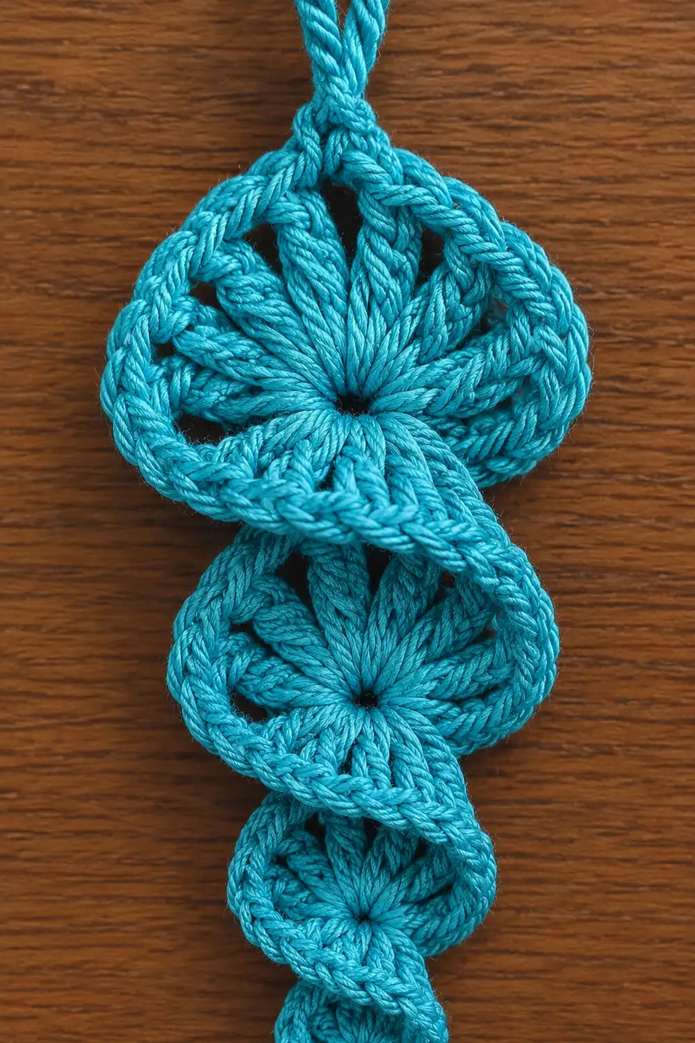 A turquoise macramé pendant with four decorative knots displayed against a wooden surface.