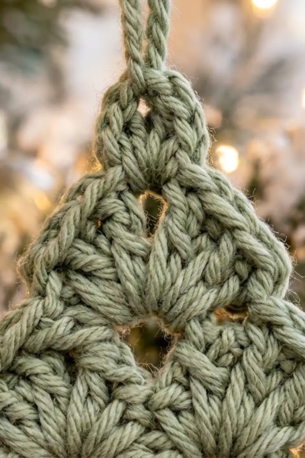 Detailed view of sage green crochet with interlocking stitches, set against warm bokeh highlights.