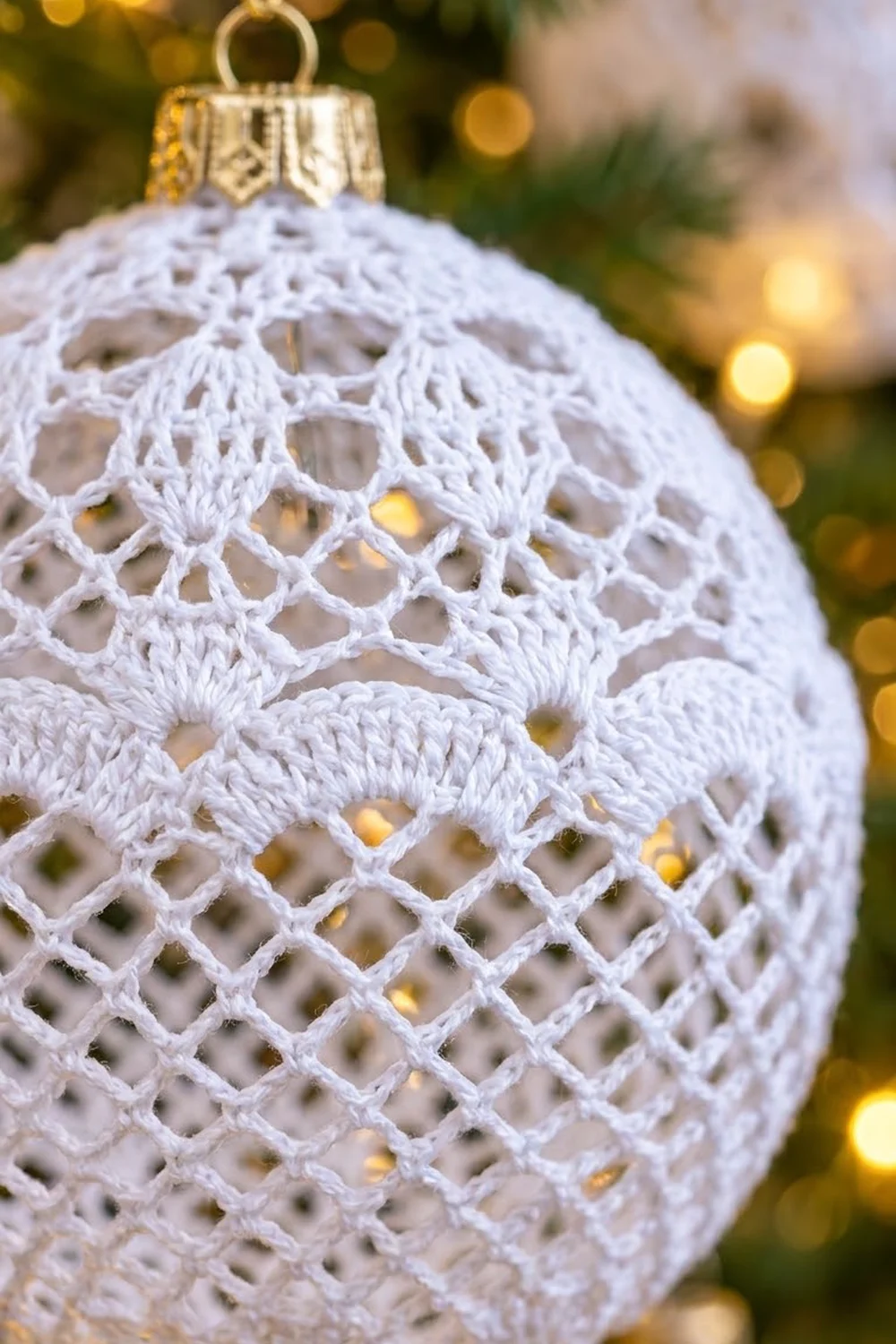 White crocheted Christmas ornament with intricate lattice pattern and gold cap, set against blurred golden bokeh lights.