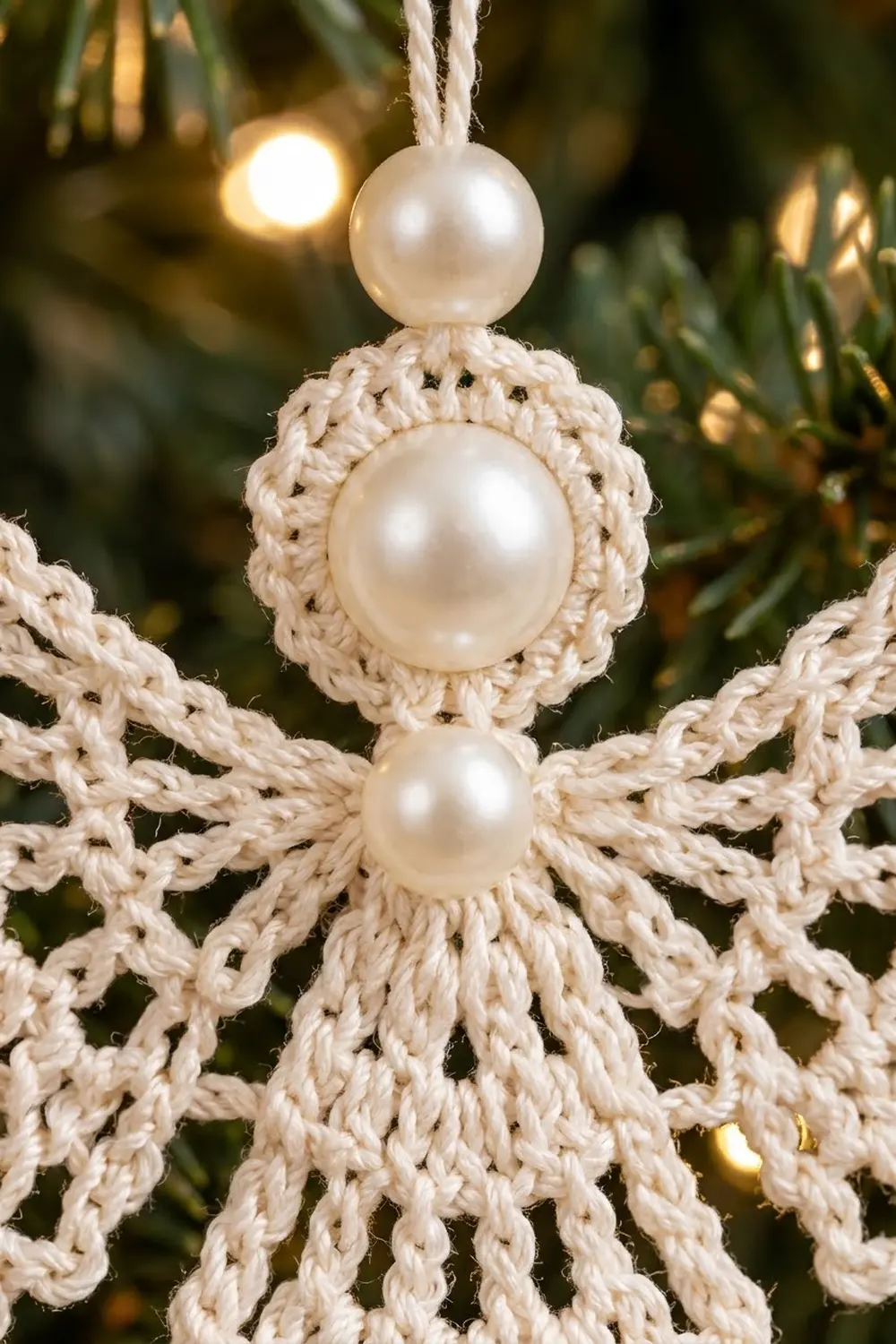 Handmade crochet star ornament with stacked pearl beads hanging among evergreen branches and warm bokeh lights.