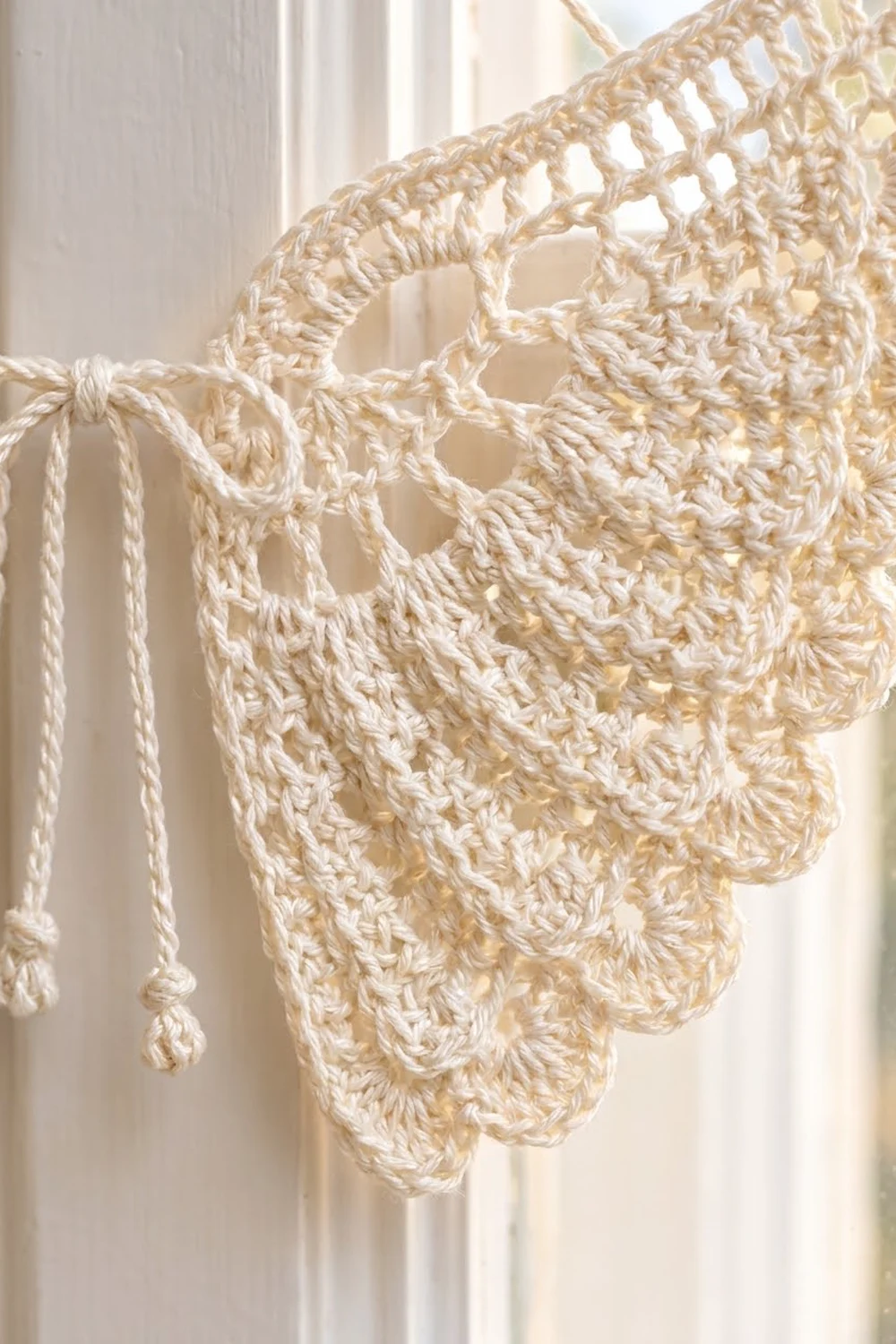 Cream-colored crocheted shawl with intricate lace openwork and delicate fringe ties, photographed in warm natural light.