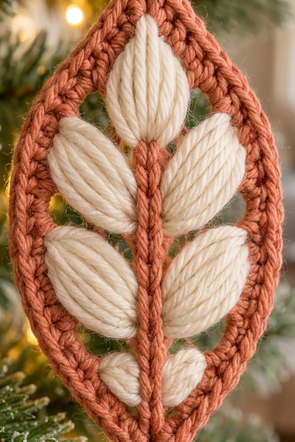 Off-white crochet petals arranged in a leaf shape, framed by rust-colored braided border, styled with warm golden bokeh.