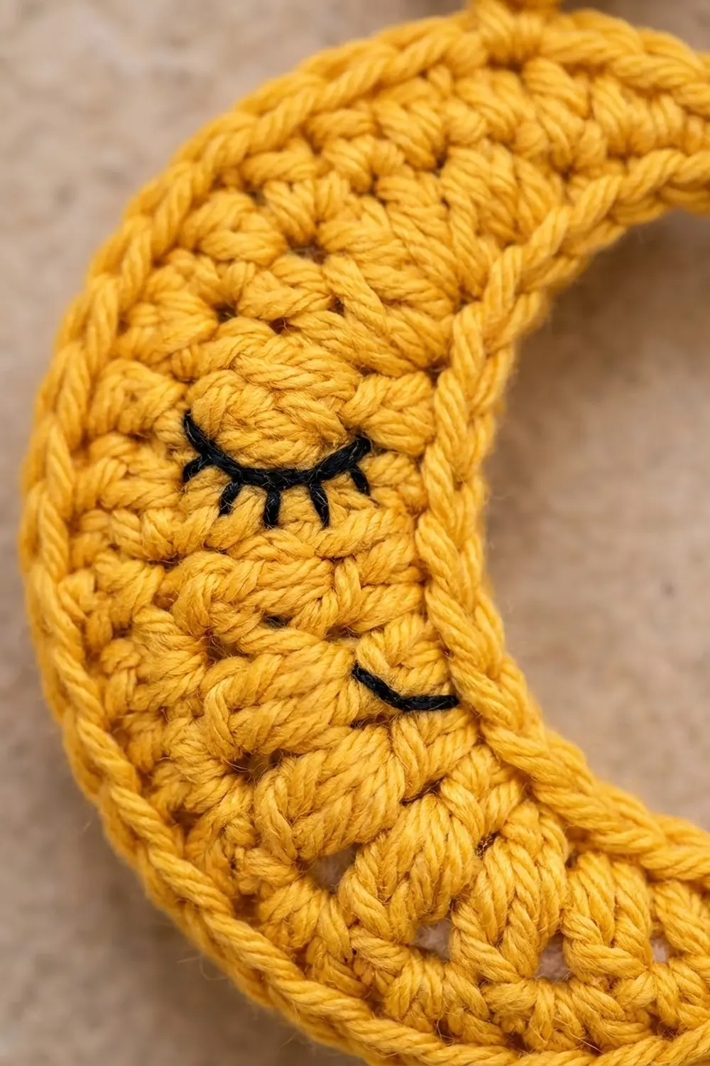 Golden crocheted fabric showing detailed stitches with black embroidered closed eyelashes against a soft blurred background.