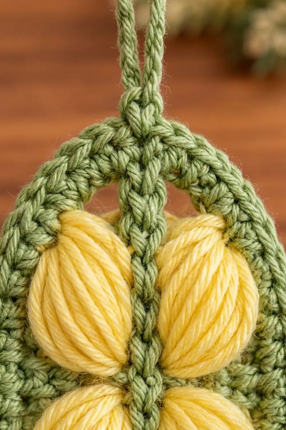 Sage green crocheted basket structure cradling wrapped yellow yarn elements, with intricate stitch detail against a soft, blurred background.