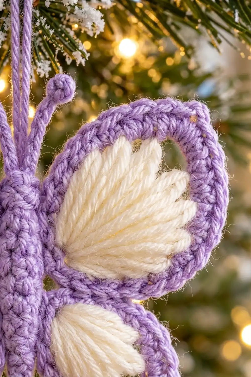 Close-up of purple and cream crocheted flower ornament with soft bokeh lights and evergreen garland in background.