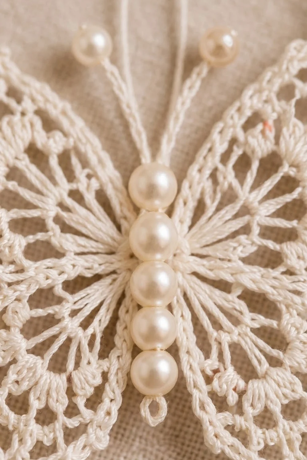 Cream-colored crocheted lace with stacked pearl beads forming a vertical line through delicate openwork pattern.