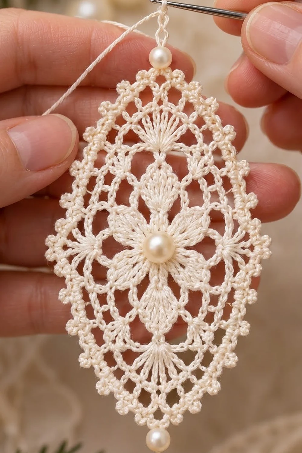A delicate cream crochet pendant with pearl beads and intricate openwork, held carefully in hands.