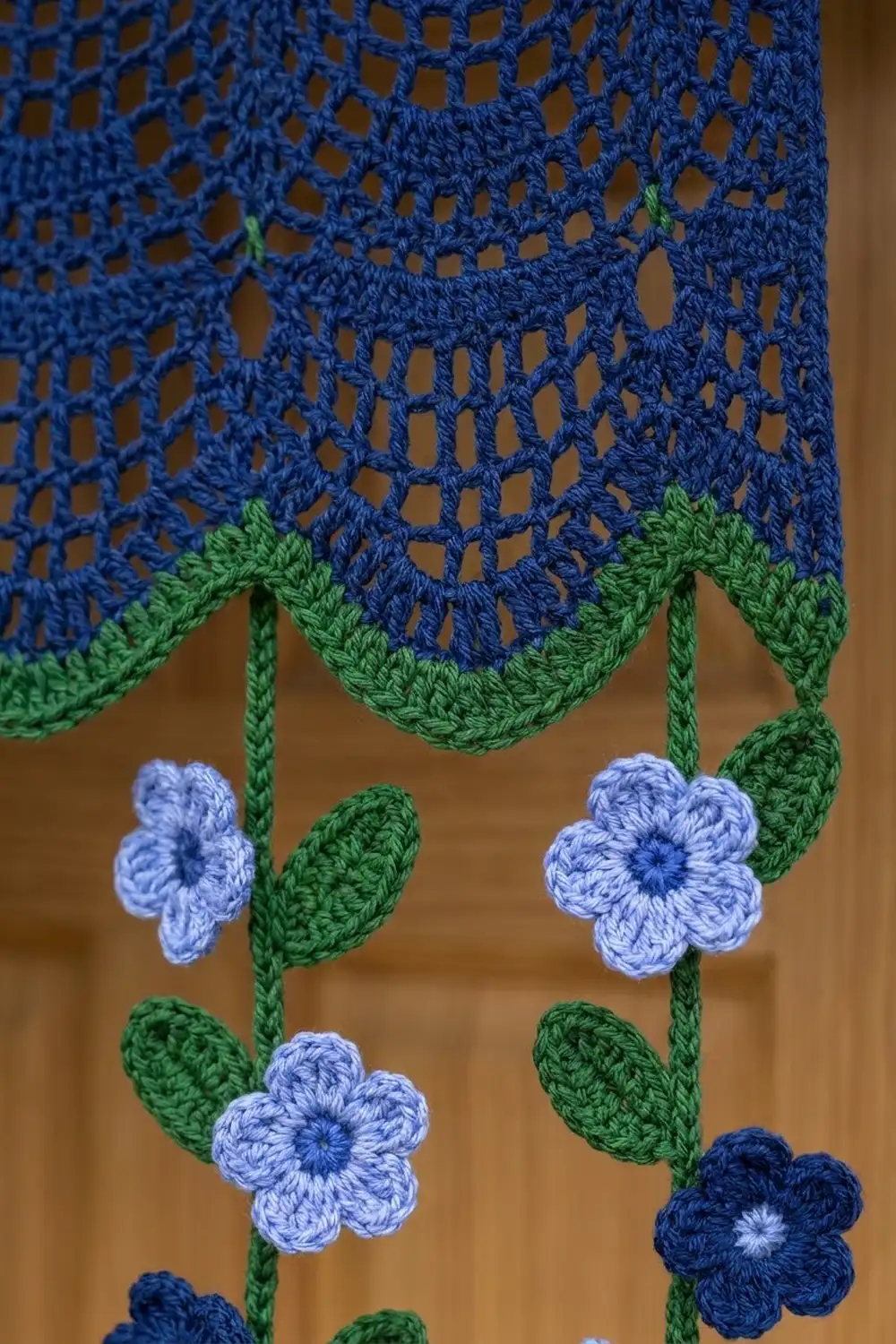 Close-up of blue crocheted lace with hanging pale blue and navy flowers with green stems.