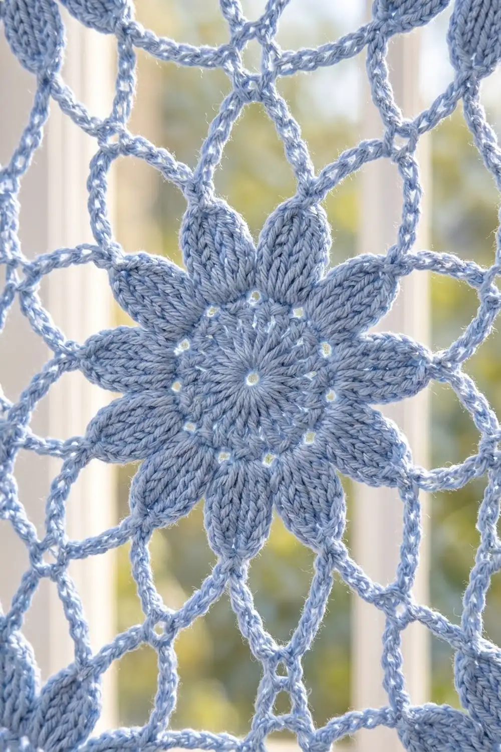 Blue crocheted flower with eight petals and beaded accents, featured in delicate geometric lace against a soft-blurred garden background.