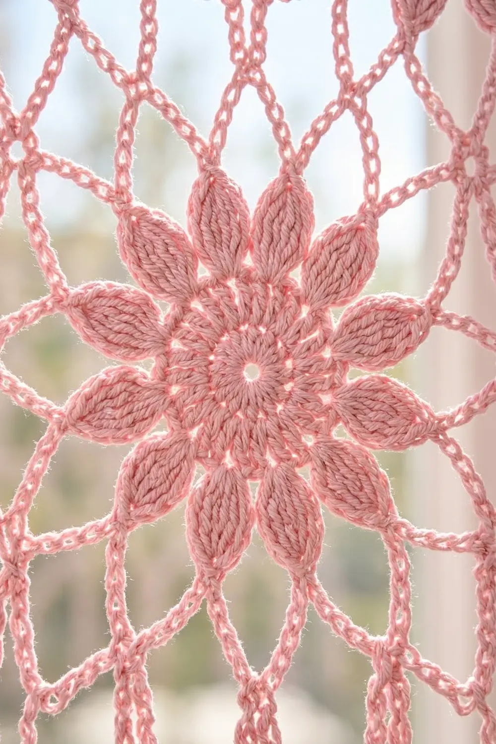 Close-up of a pink crochet flower with textured petals and chain links against a soft, blurred background.