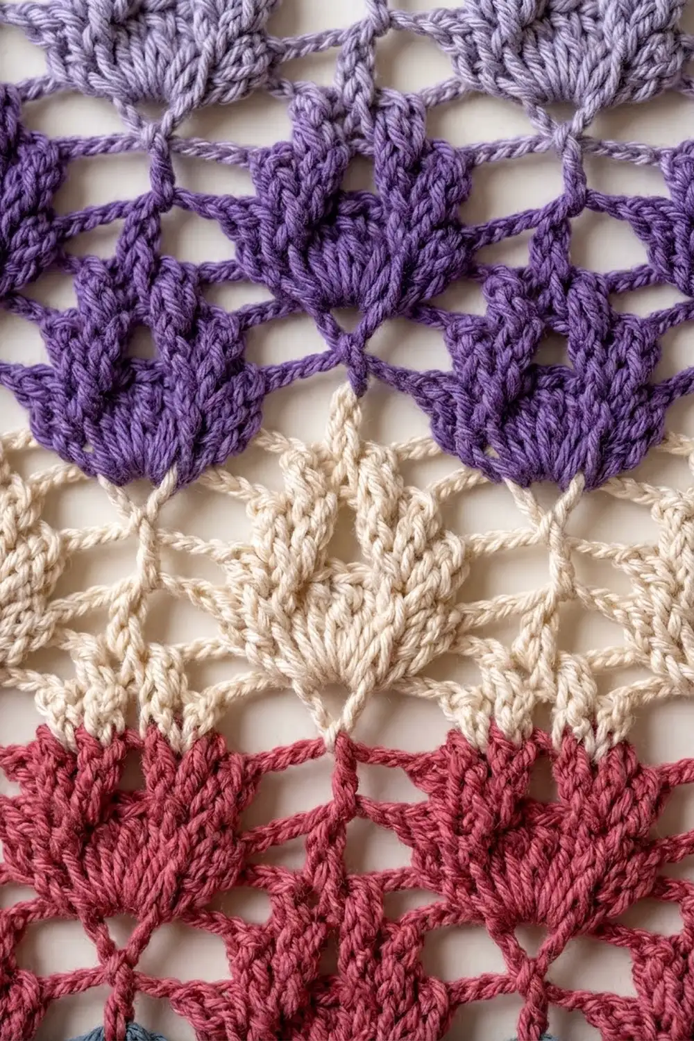 Purple, cream, and pink crochet stitches form an openwork geometric pattern with dimensional textured fibers.