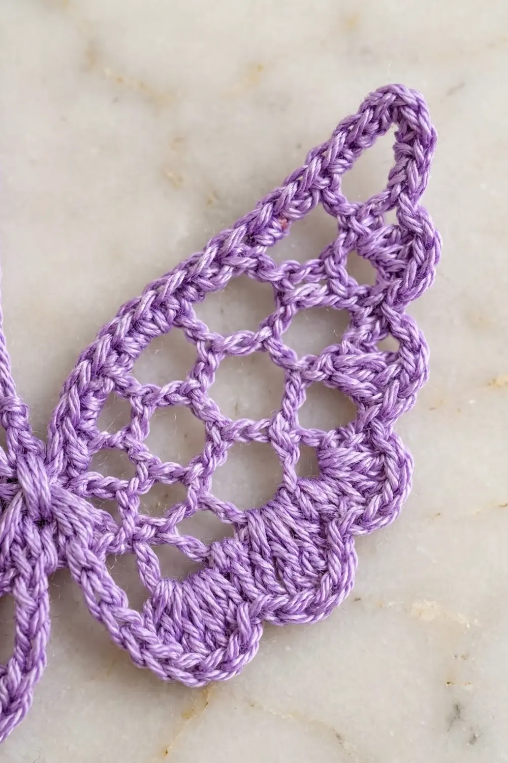 Close-up of purple crocheted lace with intricate mesh pattern on a cream-colored speckled background.