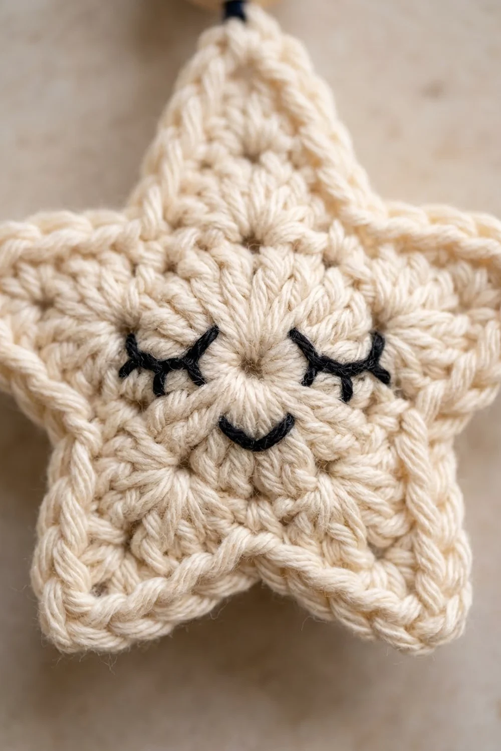 Close-up of a cream-colored crocheted star with embroidered black eyes and smile on a neutral blurred background.