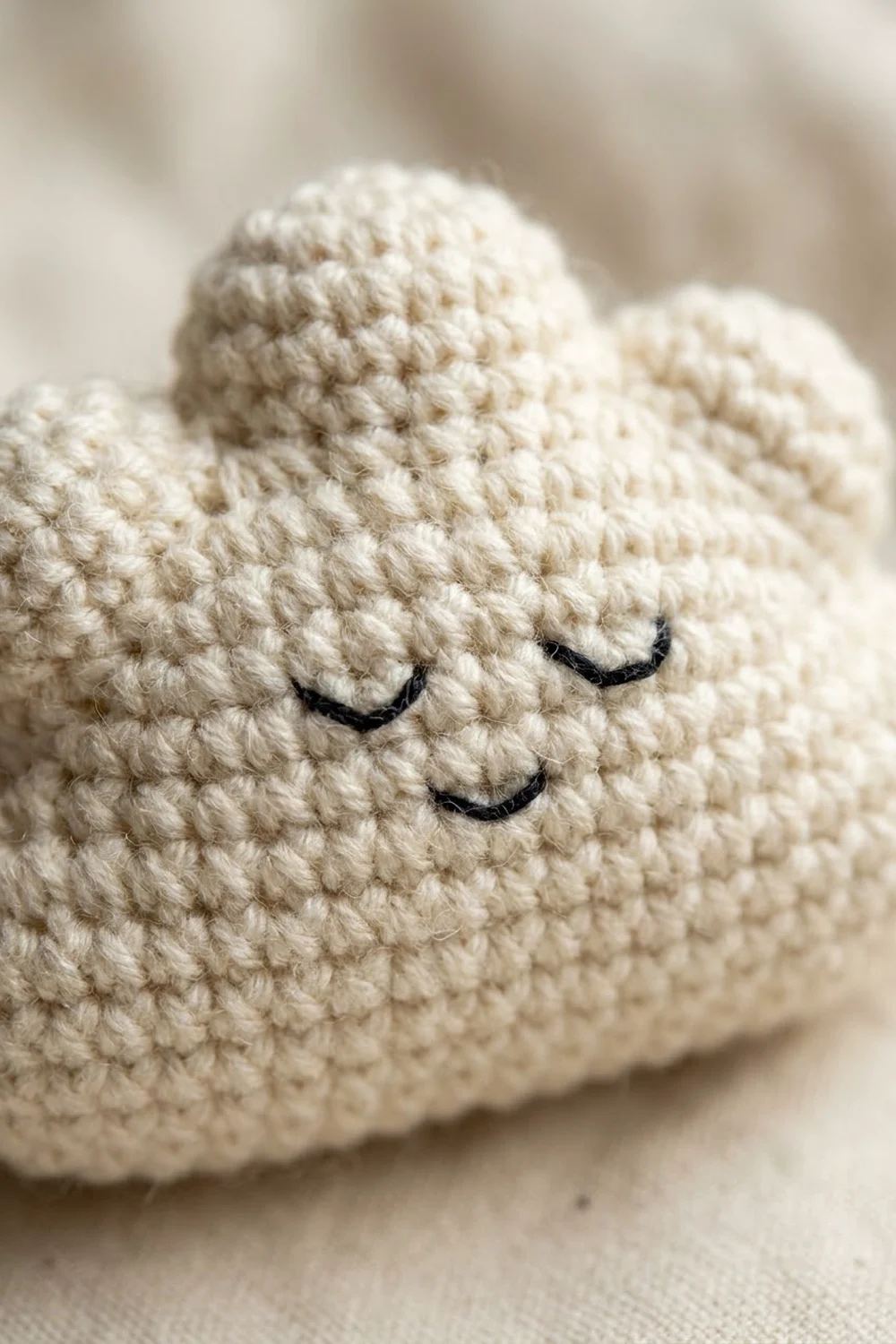 Cream-colored crocheted amigurumi with embroidered black closed eyes and gentle smile, shown in close-up detail.
