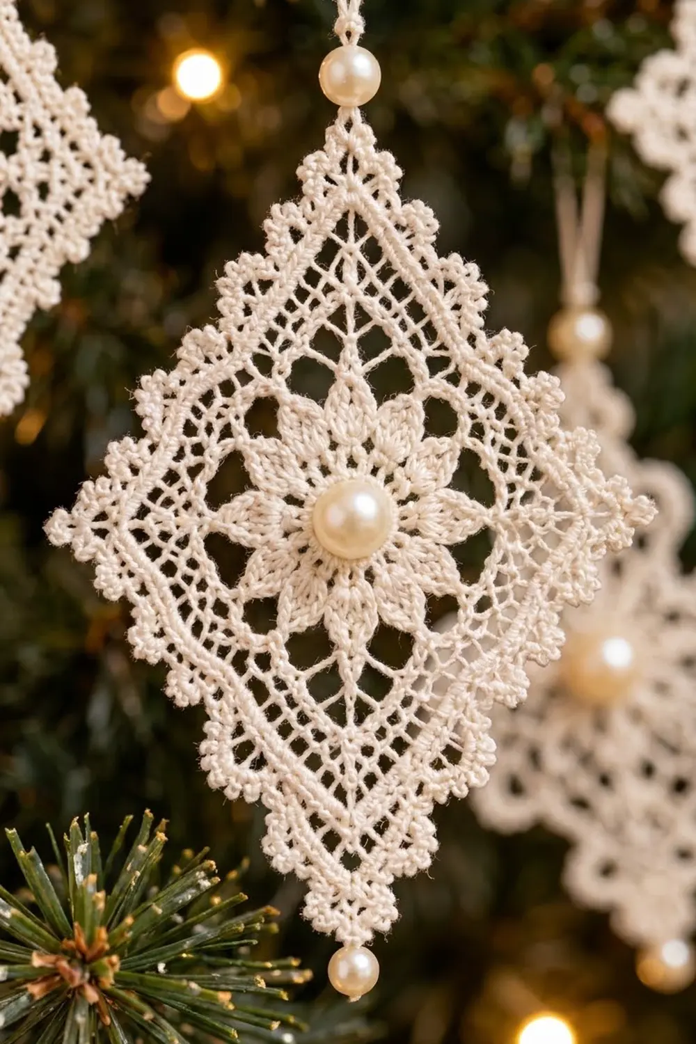 Delicate crocheted lace snowflake ornament with pearl bead center, hanging on evergreen against warm golden lights.