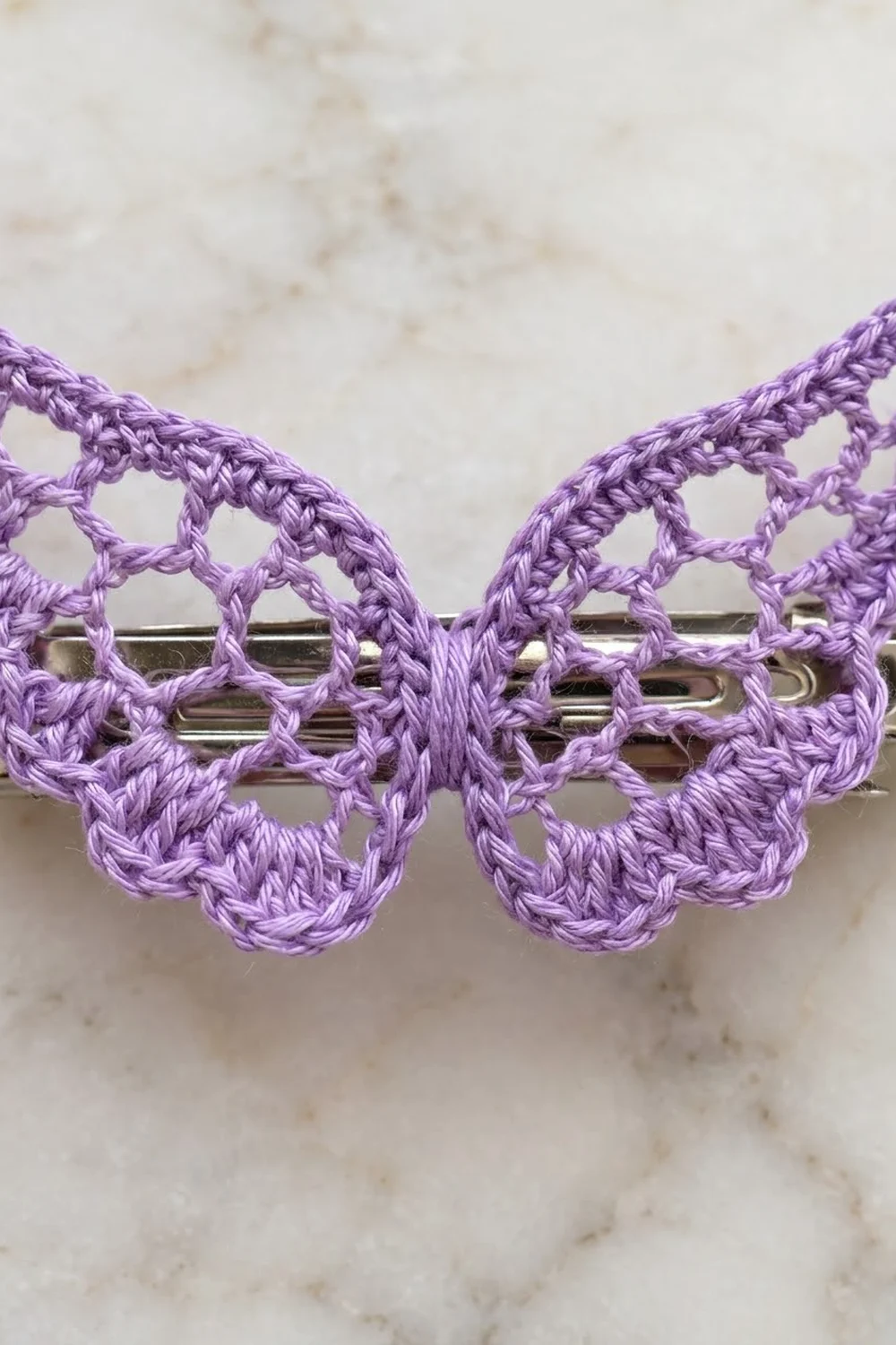 Delicate purple crochet lace with scalloped butterfly motifs strung on a silver rod, set on a cream stone surface.