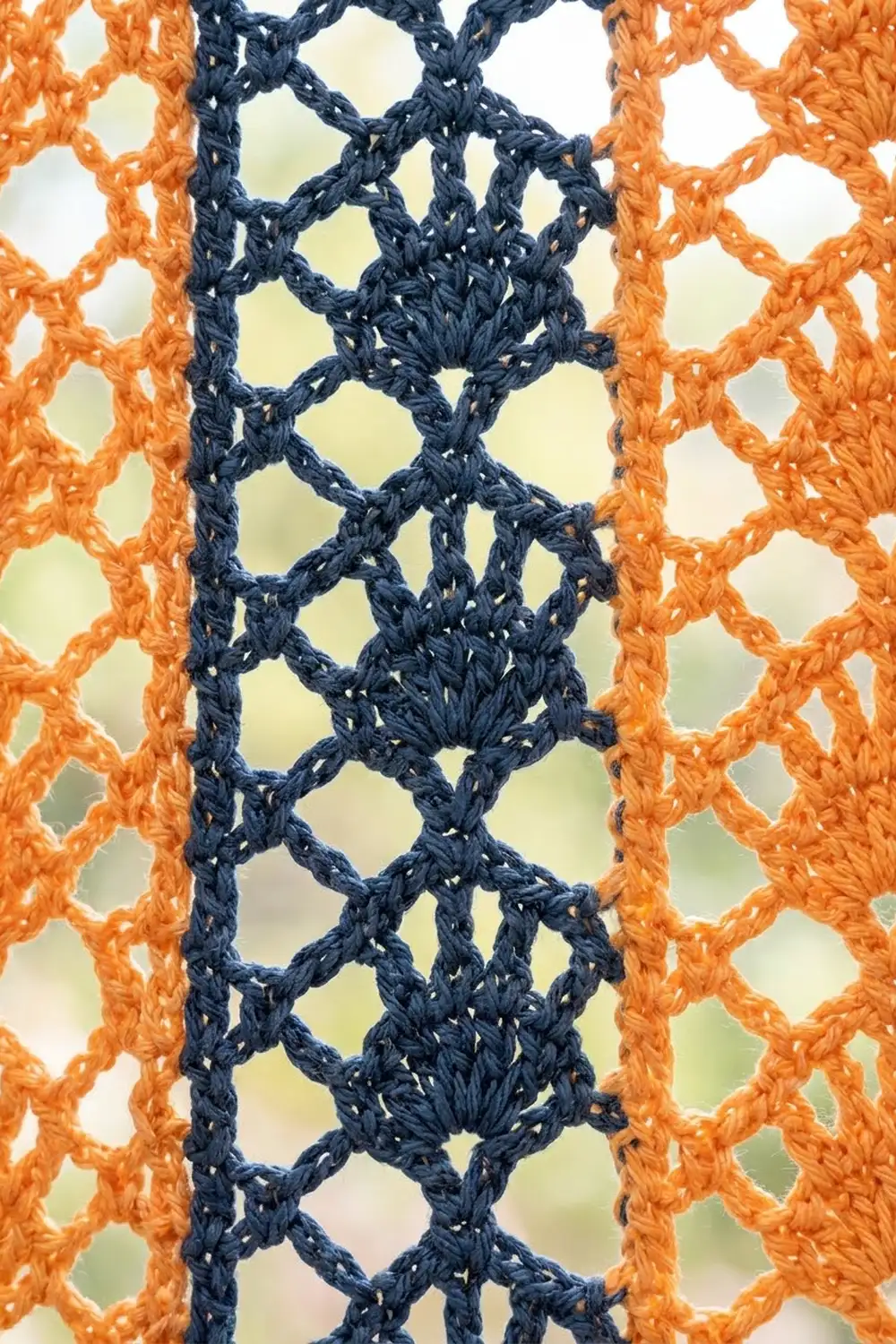 Navy blue and burnt orange crocheted lace with diamond-shaped openings, photographed against a soft blurred green background.