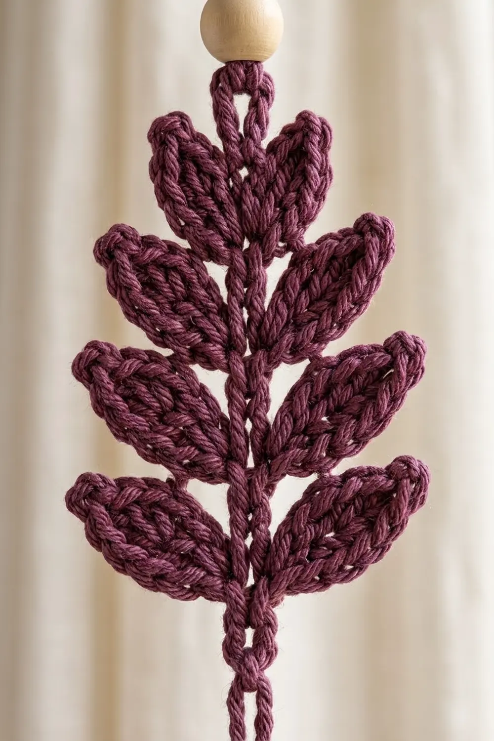 Crocheted burgundy botanical ornament with four tiers of leaf-shaped petals and natural wood top bead.