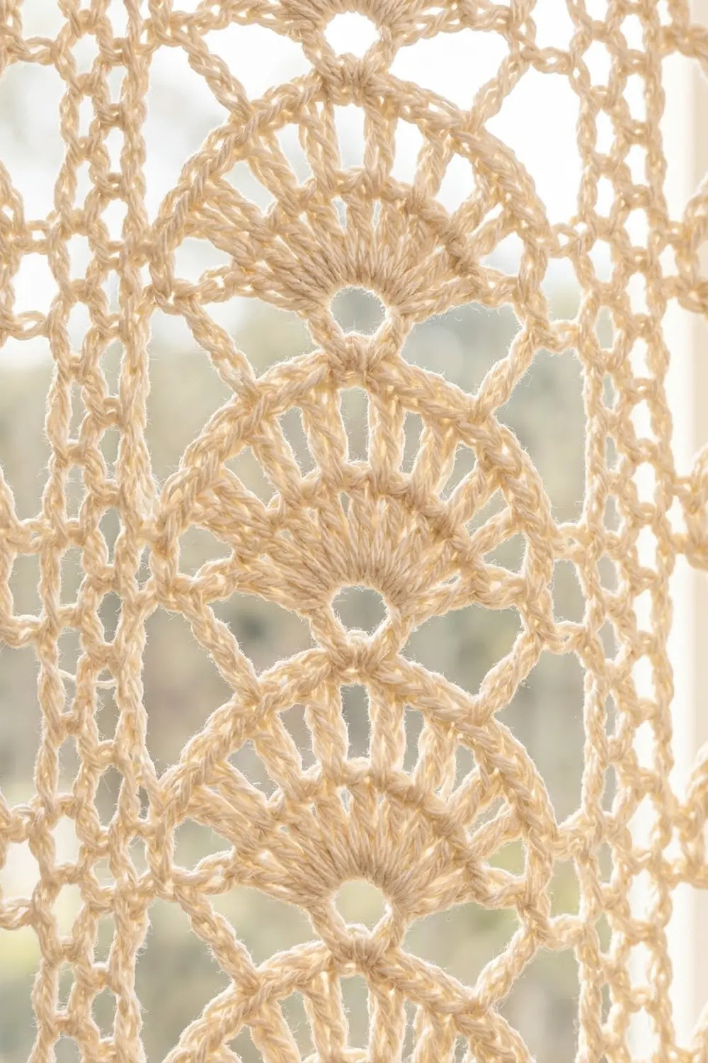 Close-up of beige crochet lace with geometric circular motifs and an openwork pattern against a blurred neutral background.