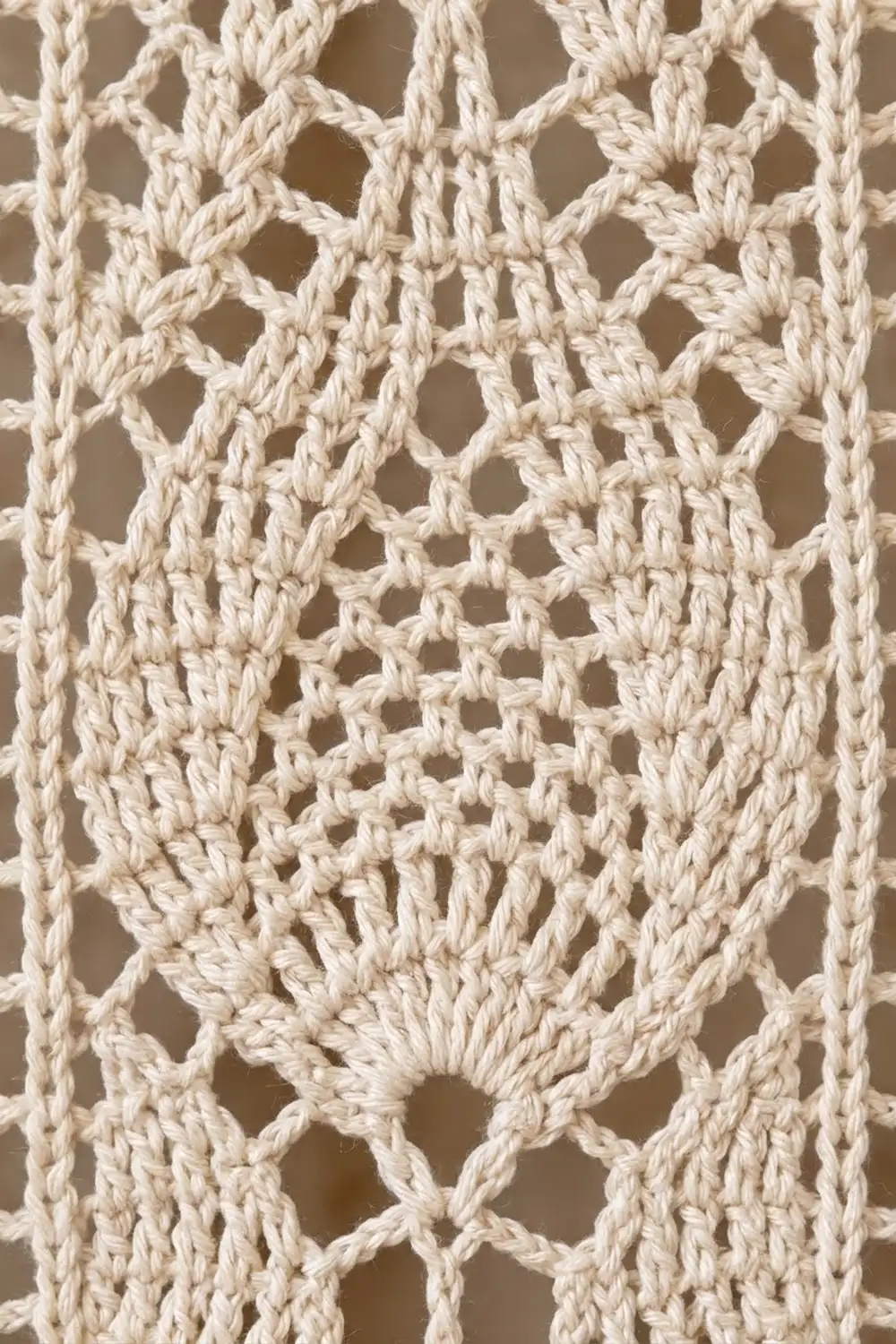 Close-up of cream crochet showing detailed open lattice stitch pattern with warm beige background showing through.