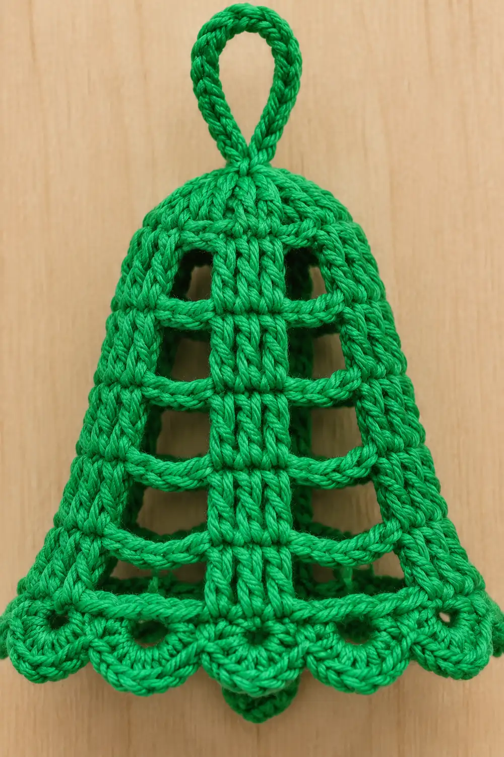 A bright green crocheted bell ornament with a lattice pattern and looped handle hangs against a light wooden background.
