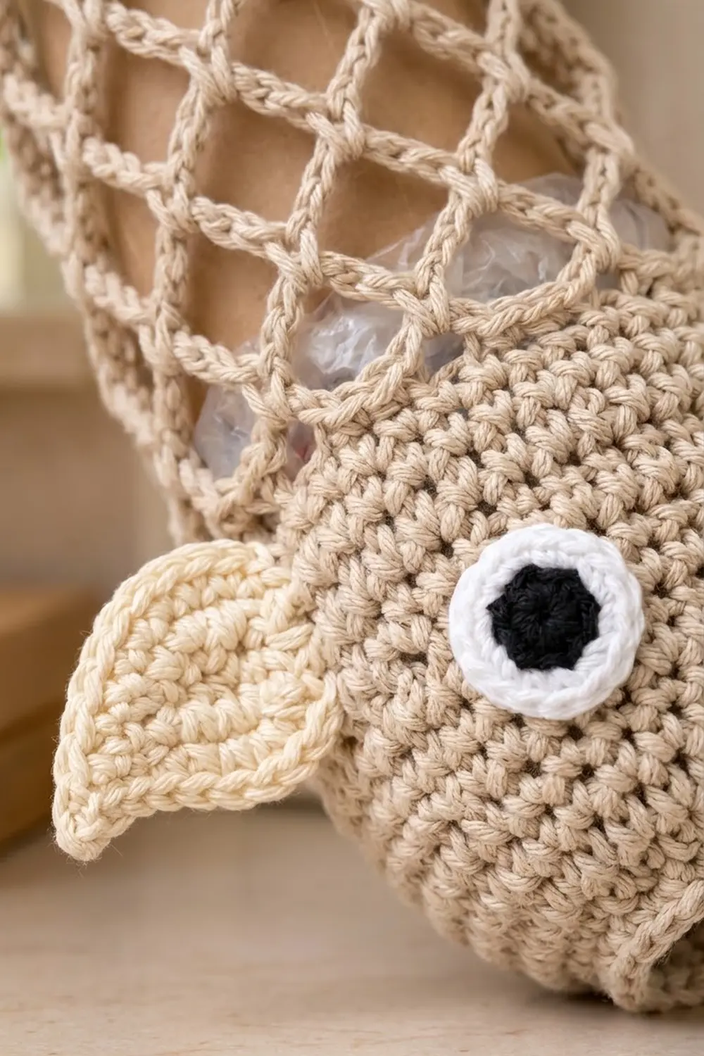 Cream-colored crocheted amigurumi with dense textured body, white safety eye with black pupil, and open-mesh lace details.
