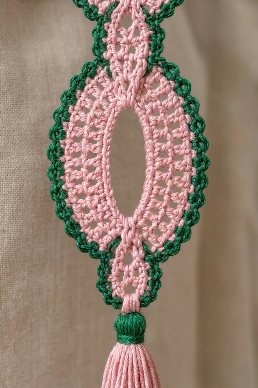 Crocheted lace bookmark in pink and green with decorative tassel, close-up showing openwork stitching on neutral background.