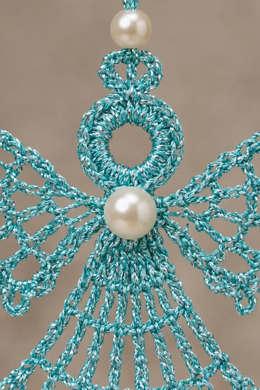 Close-up of teal speckled crochet lace with cream pearls accenting delicate openwork against gray background.
