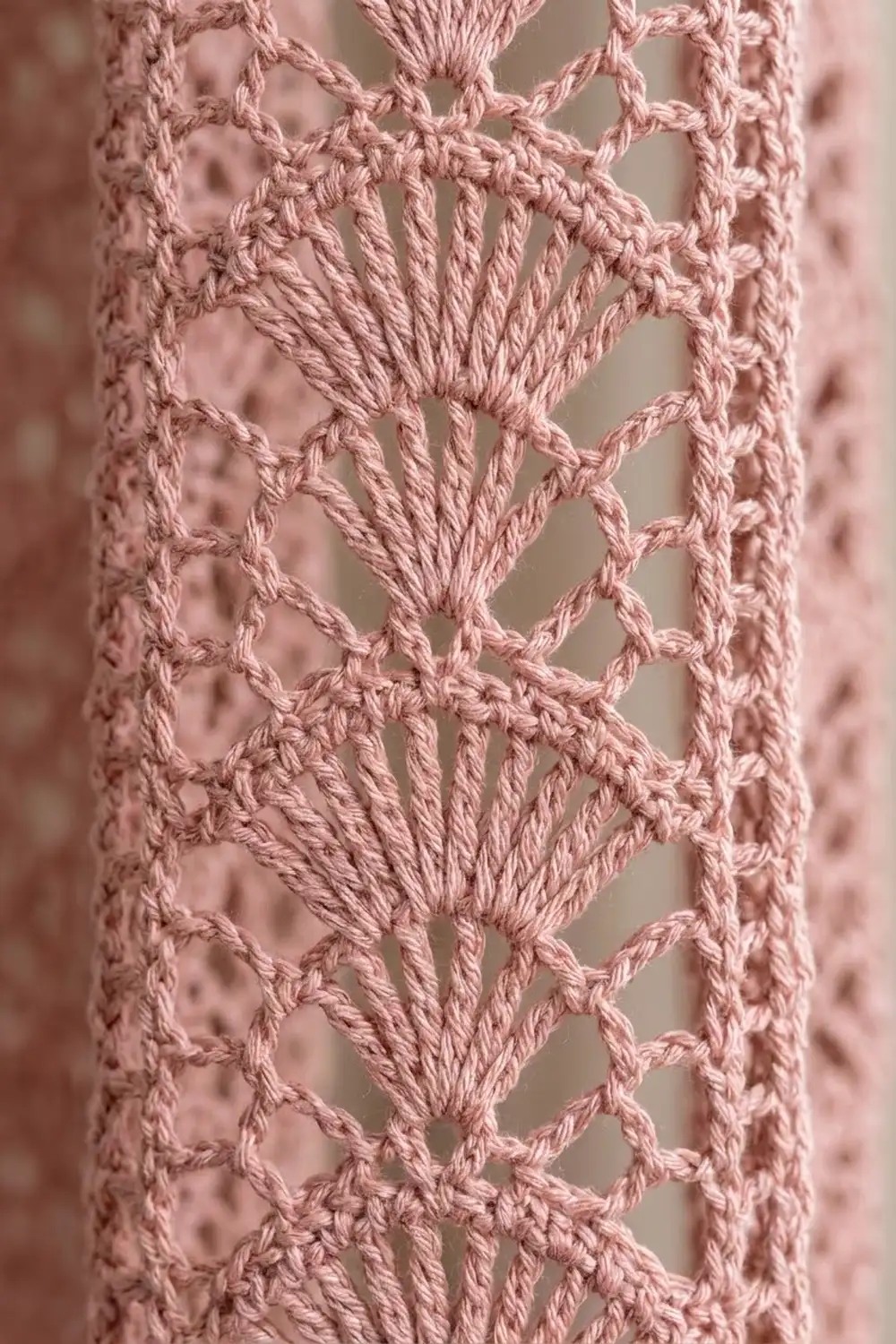 Close-up of mauve-pink crocheted lace with repeating chevron stitch pattern and visible rope texture detail.