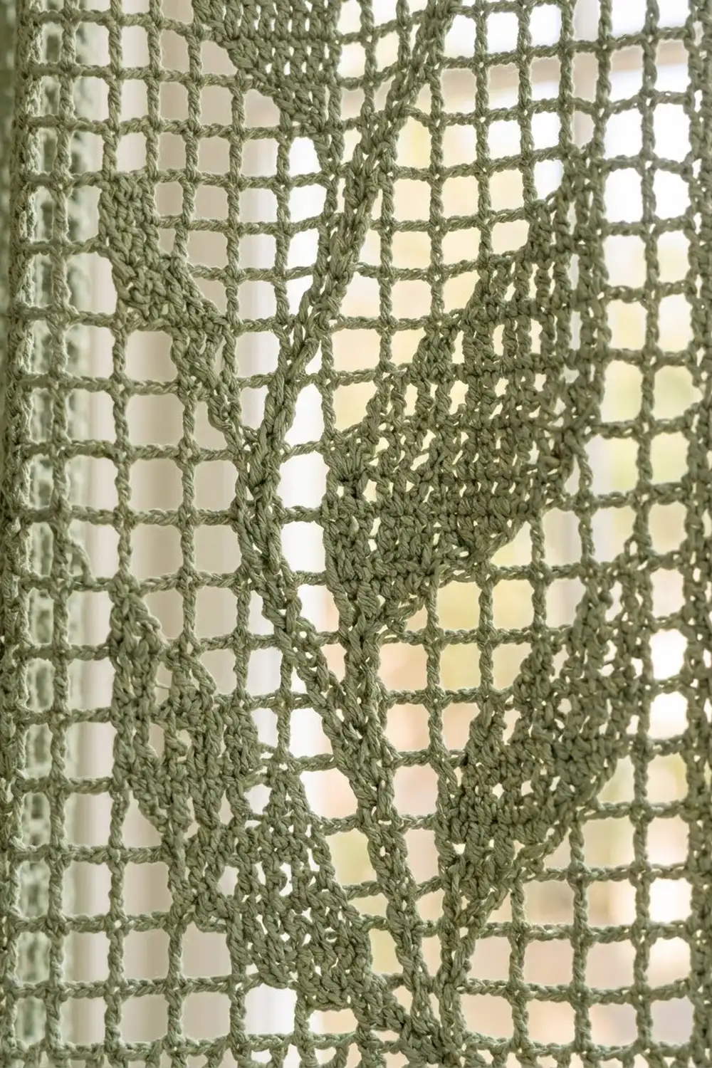 Layered sage-green crocheted fabric with open geometric mesh pattern showing texture and dimensional folds.