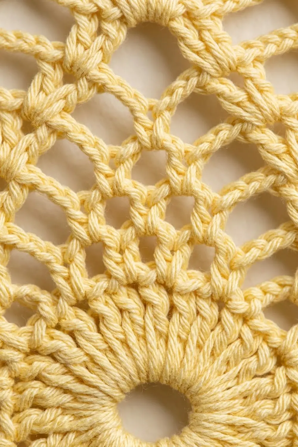 Pale yellow crocheted lattice mesh with twisted stitches creating a diamond pattern against a soft cream background.