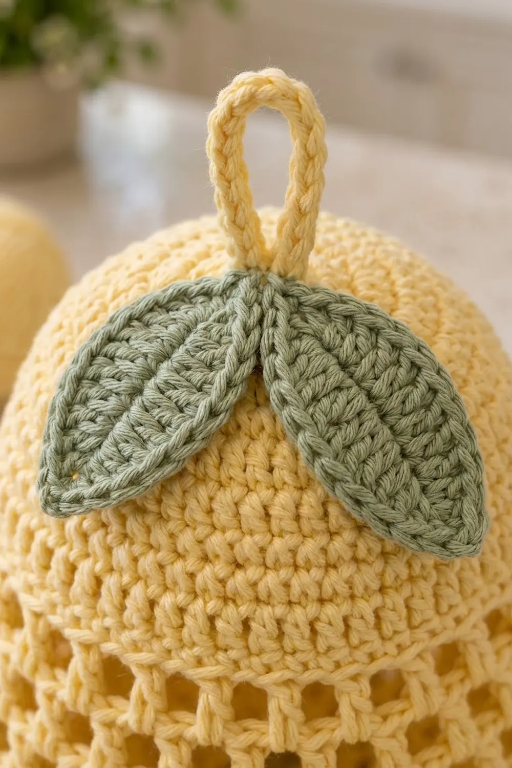 Crocheted yellow lemon with green leaves and braided rope handle detail.