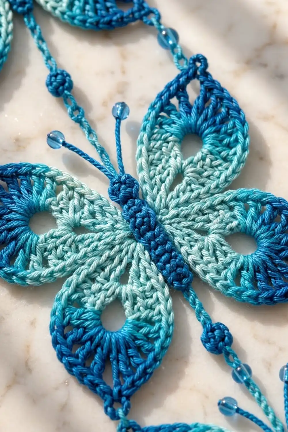Crocheted teardrop ornaments in blue and mint green yarn with beaded strings on a marble background.