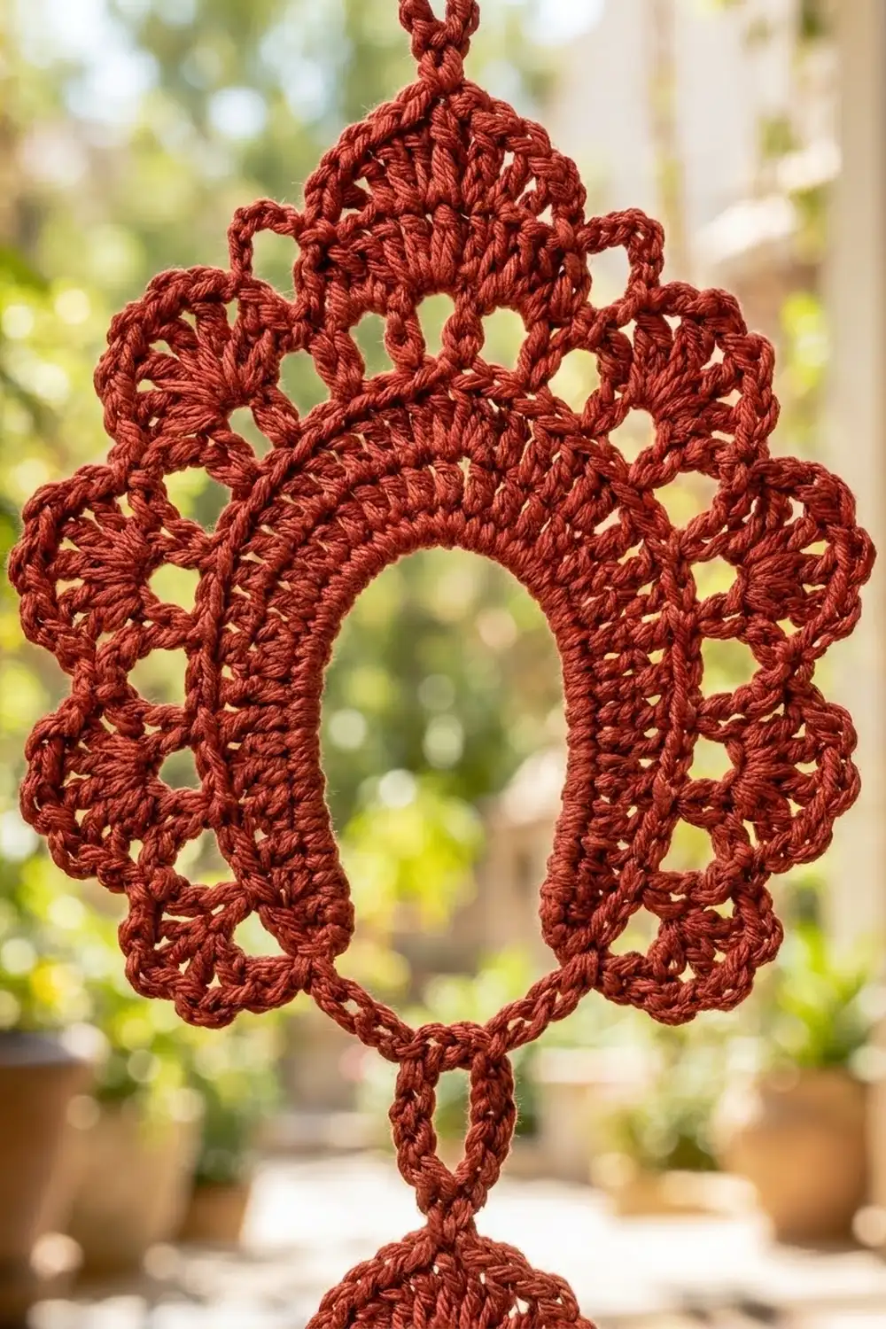 Burgundy crocheted lace ornament with intricate snowflake pattern, held against a blurred green garden background.