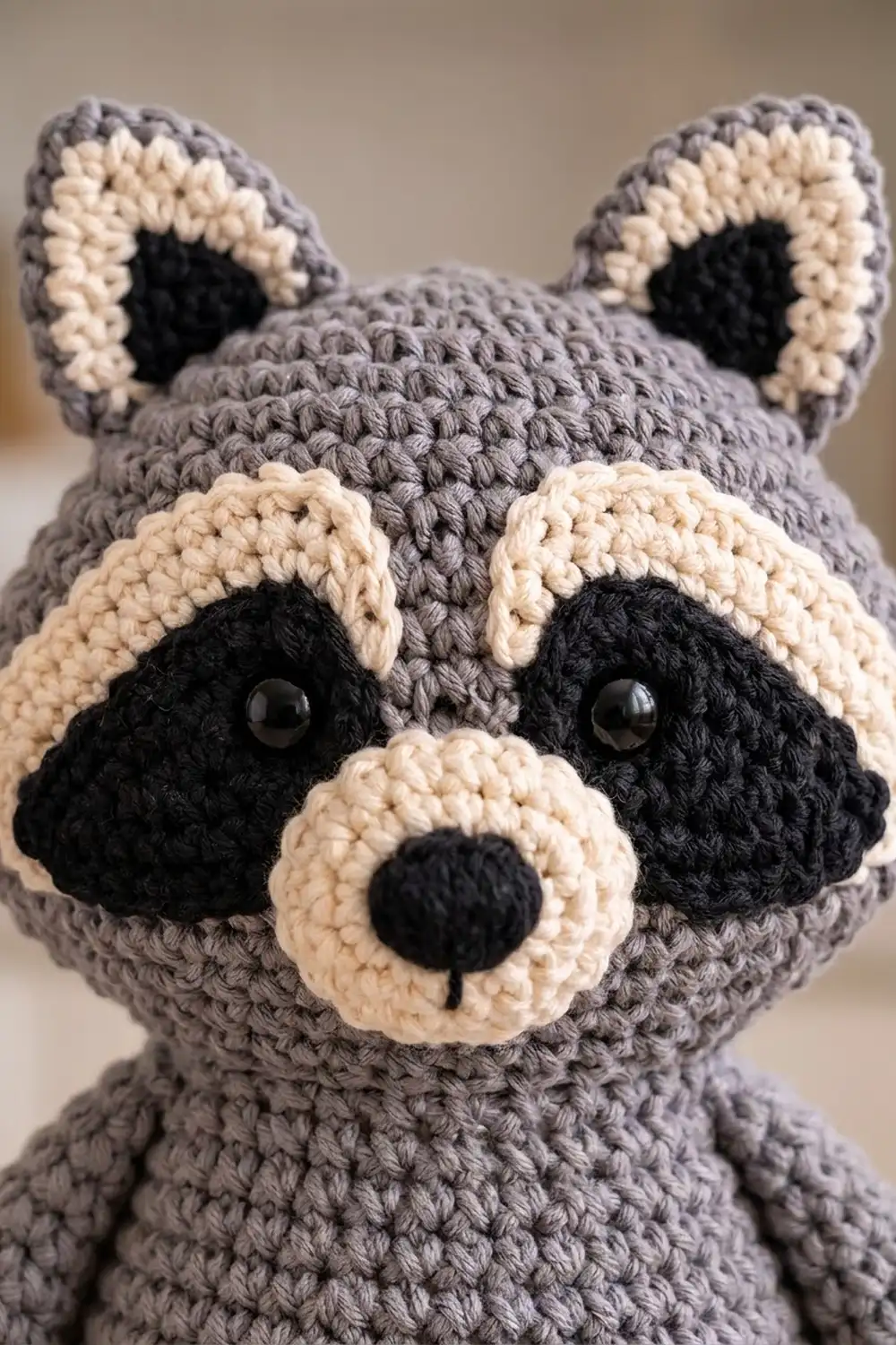 Crocheted gray raccoon with cream-colored face markings, black button eyes, and embroidered nose detail.
